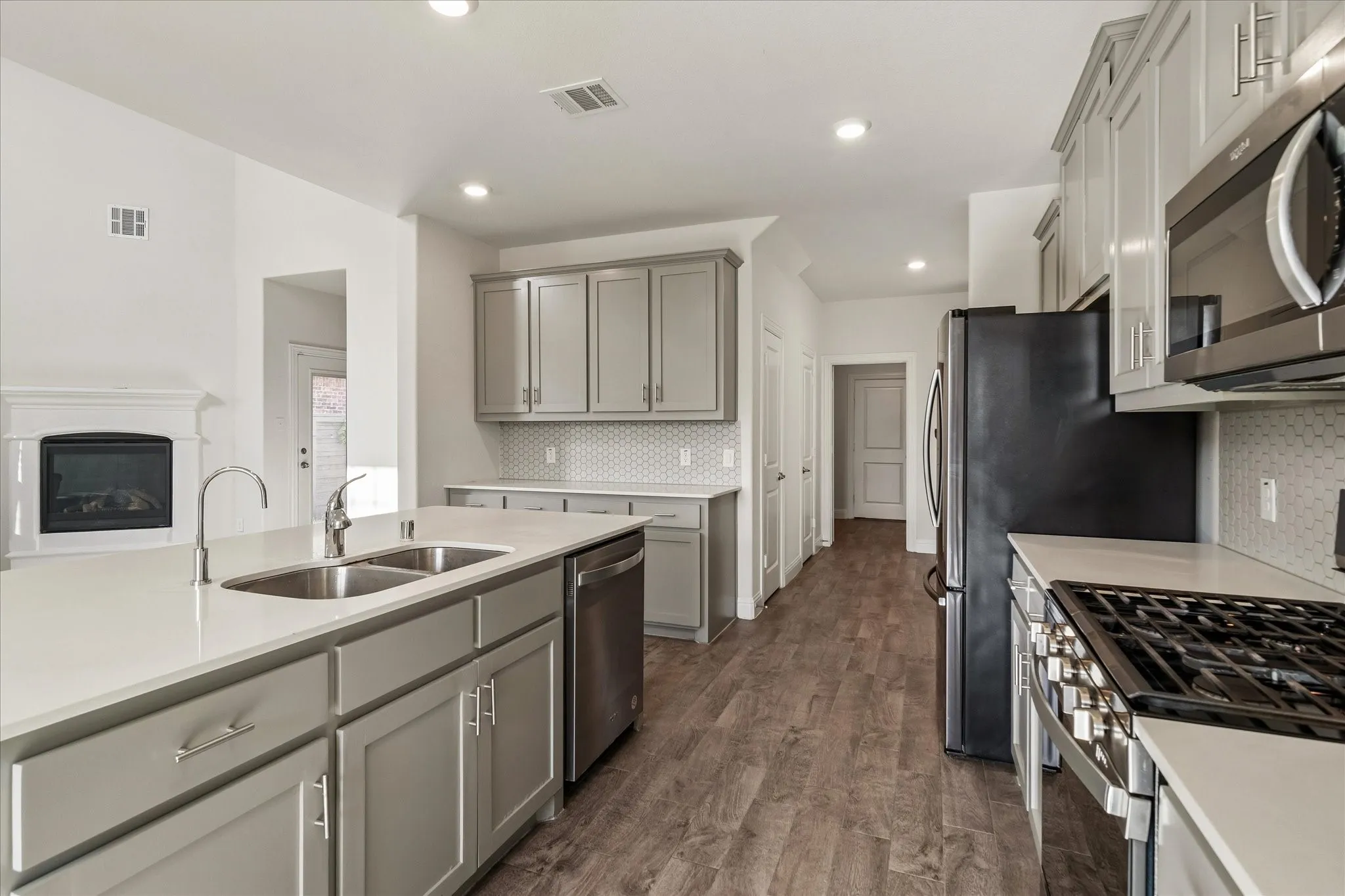 Kitchen featuring gray cabinetry, stainless steel appliances, a center island with double sink, and wood-finish flooring