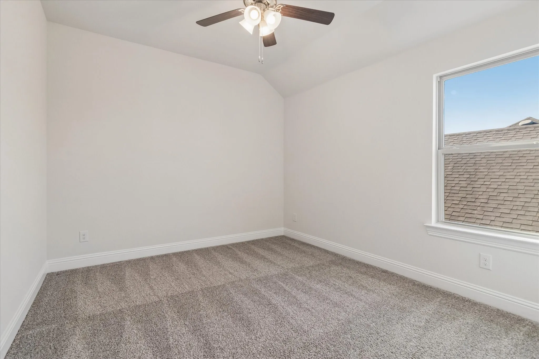 Vaulted ceiling with an attached ceiling fan, large window with white trim, and gray carpet flooring