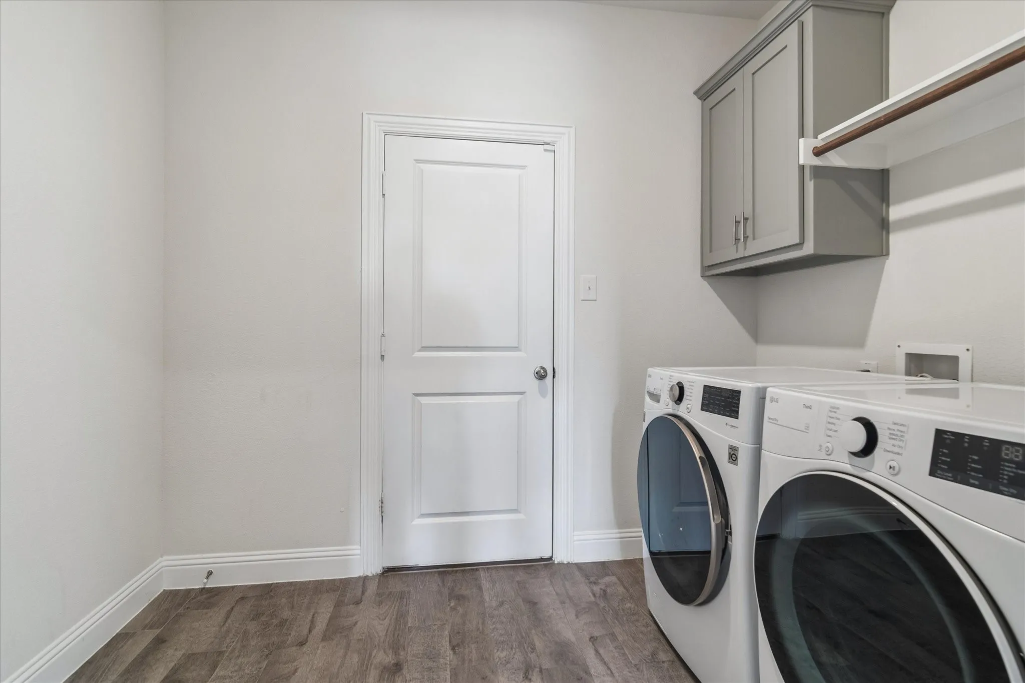 Wood-finish flooring, white paneled door, built-in gray cabinetry, and laundry hookups