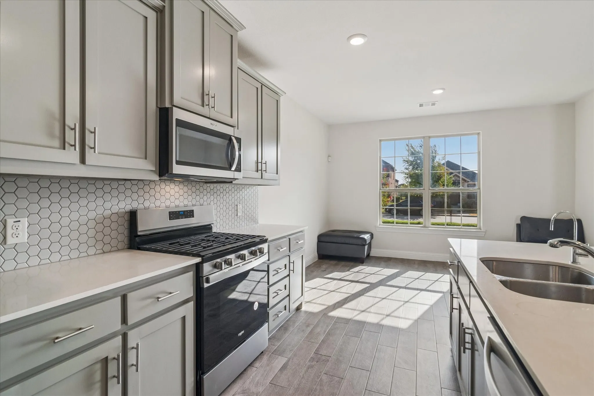 Kitchen featuring stainless steel appliances, light gray cabinetry, a hexagonal tile backsplash, light-toned countertops, and wood-finish flooring