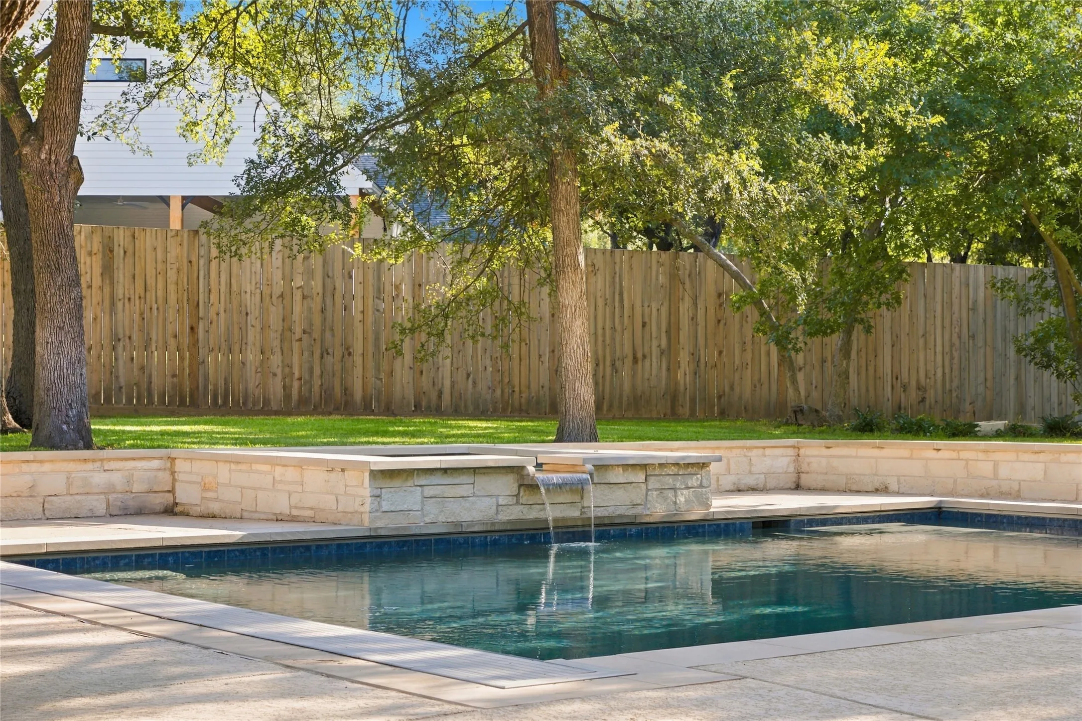 Outdoor swimming pool with integrated spa and waterfall feature, surrounded by concrete decking and stone retaining walls
