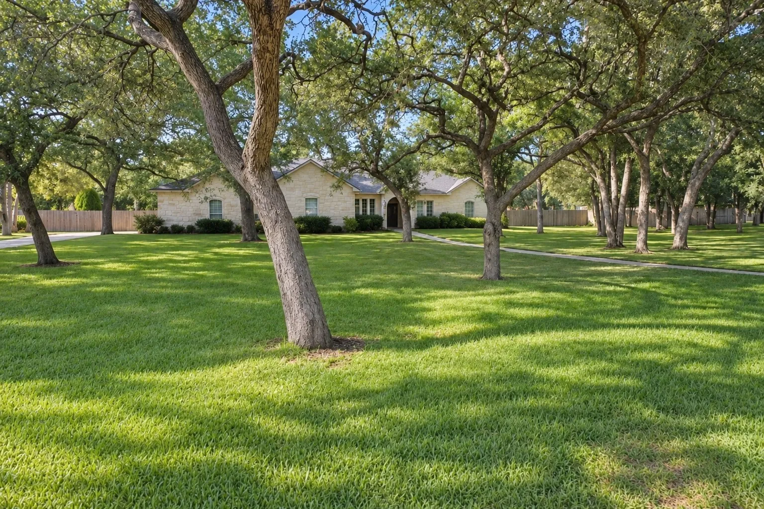 Expansive front lawn with mature trees, a stone exterior, and a paved walkway