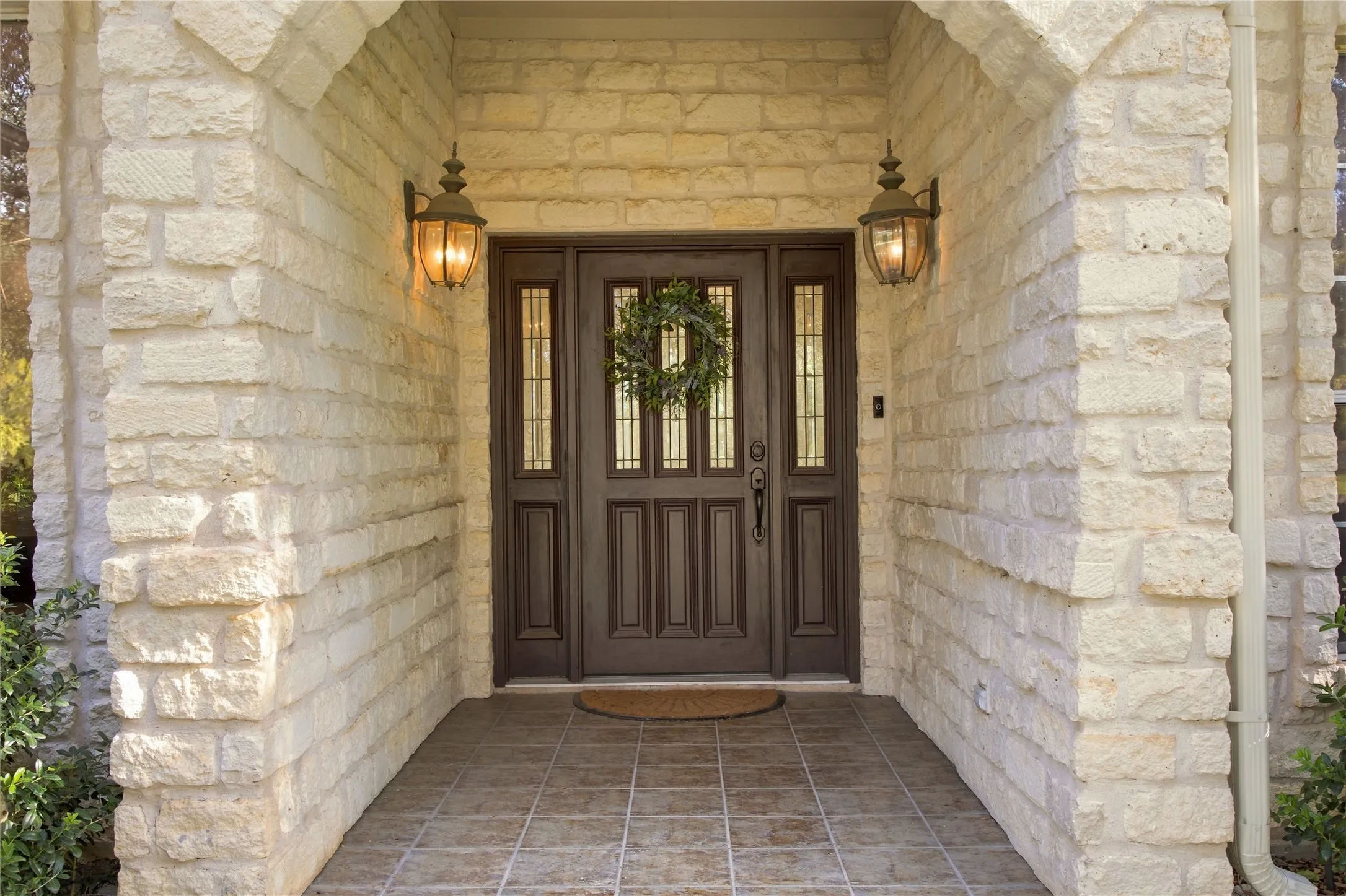 Stone exterior with a double entry door featuring sidelights, overhead transom windows, and wall-mounted exterior light fixtures