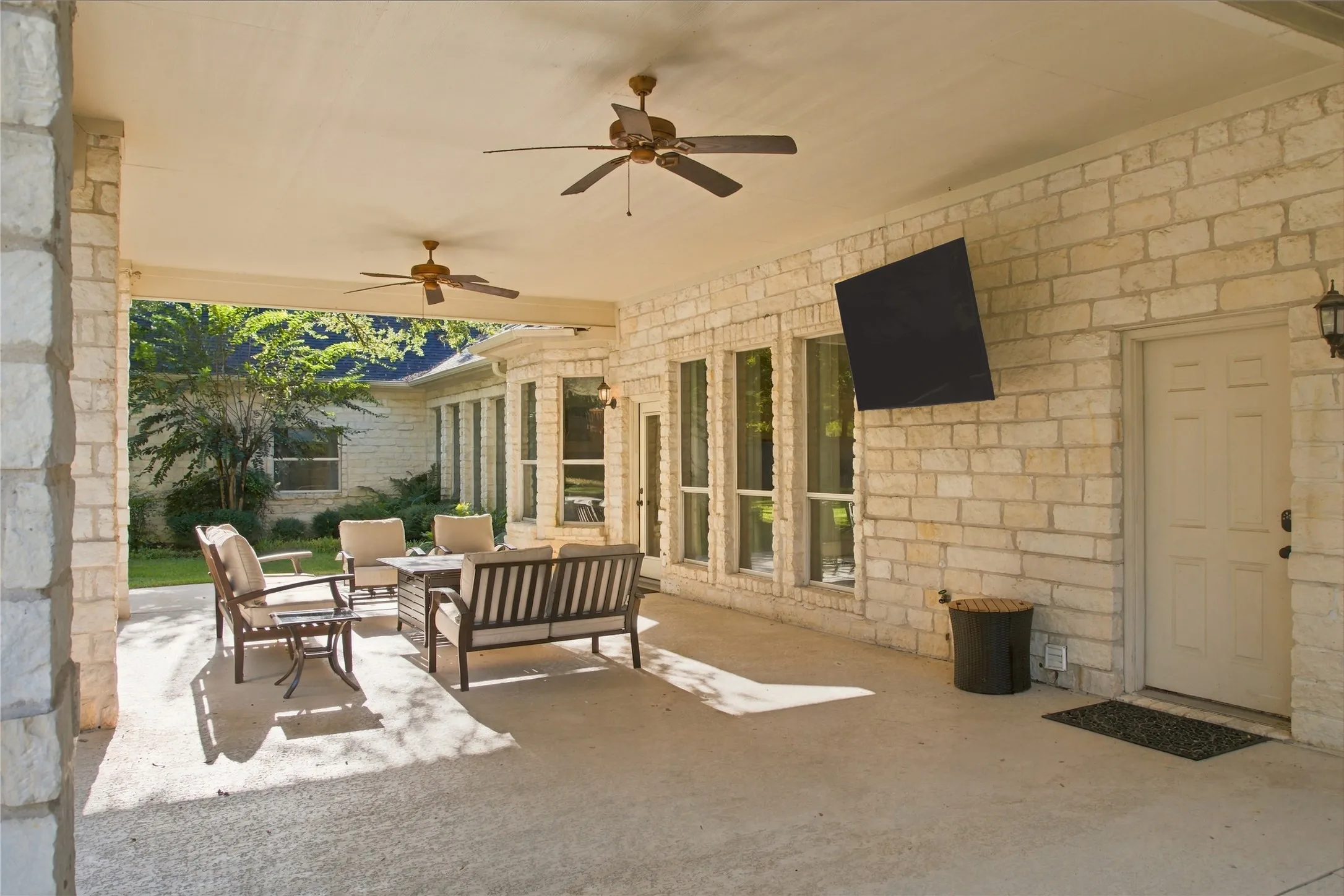 Expansive covered patio featuring a concrete surface, stone exterior walls, and ceiling fans