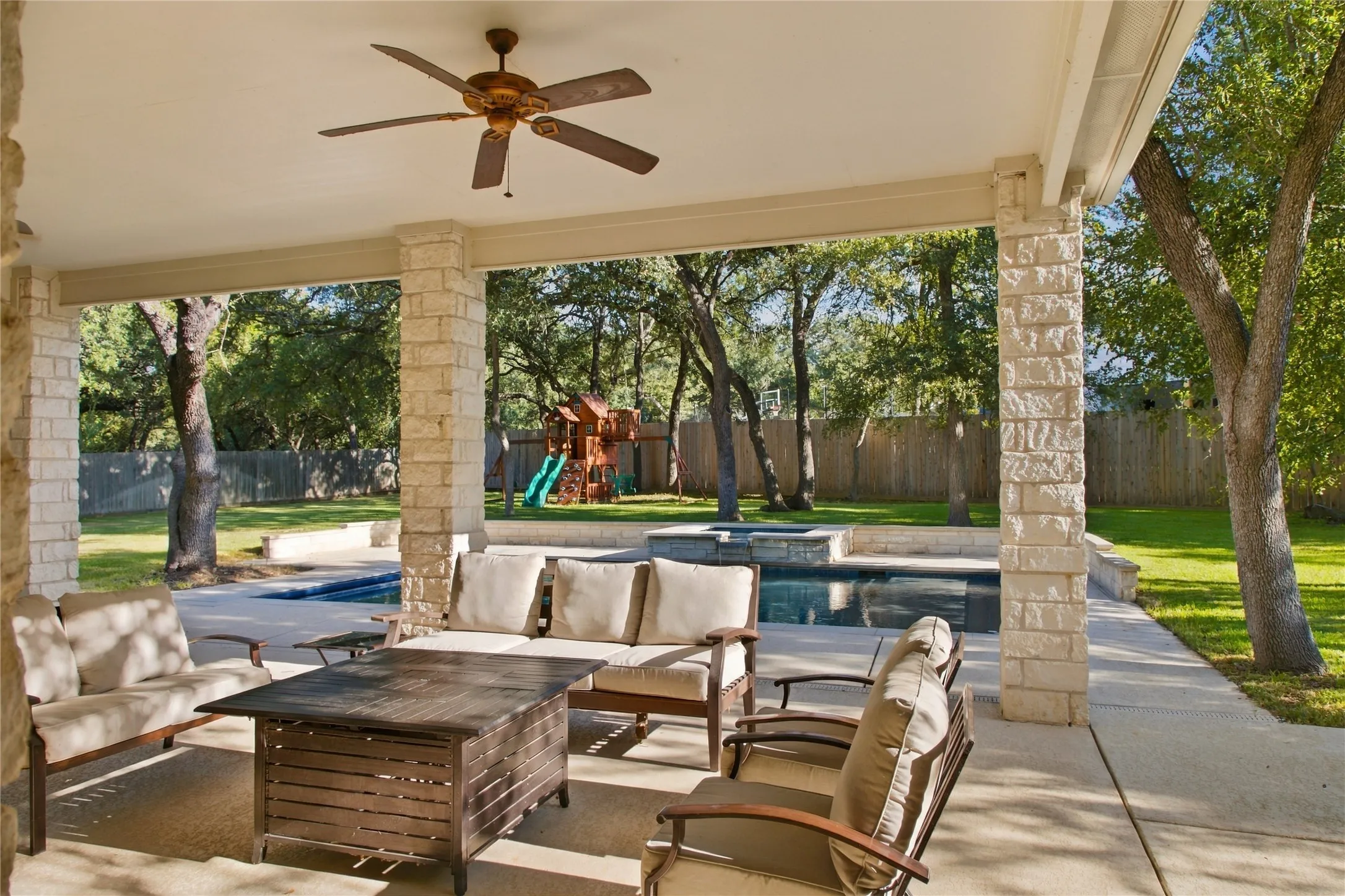 Covered patio with stone columns, ceiling fan, concrete flooring, and a swimming pool