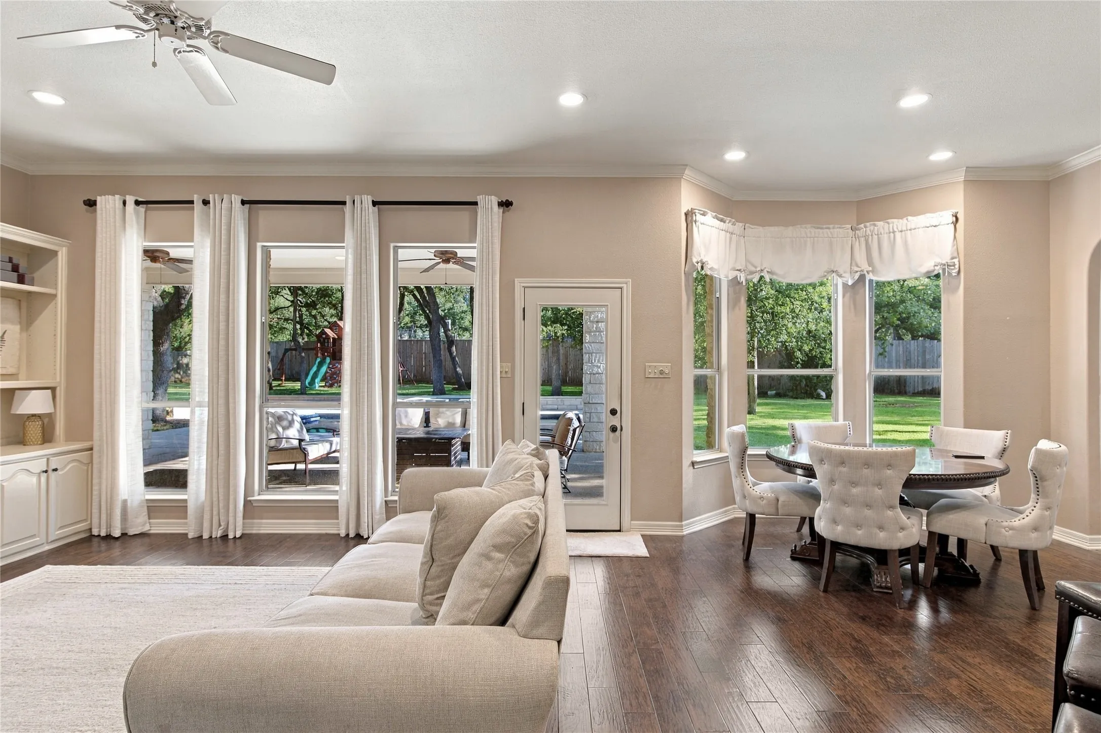 Recessed lighting, crown molding, built-in shelving, wood-finish flooring, and bay window dining area