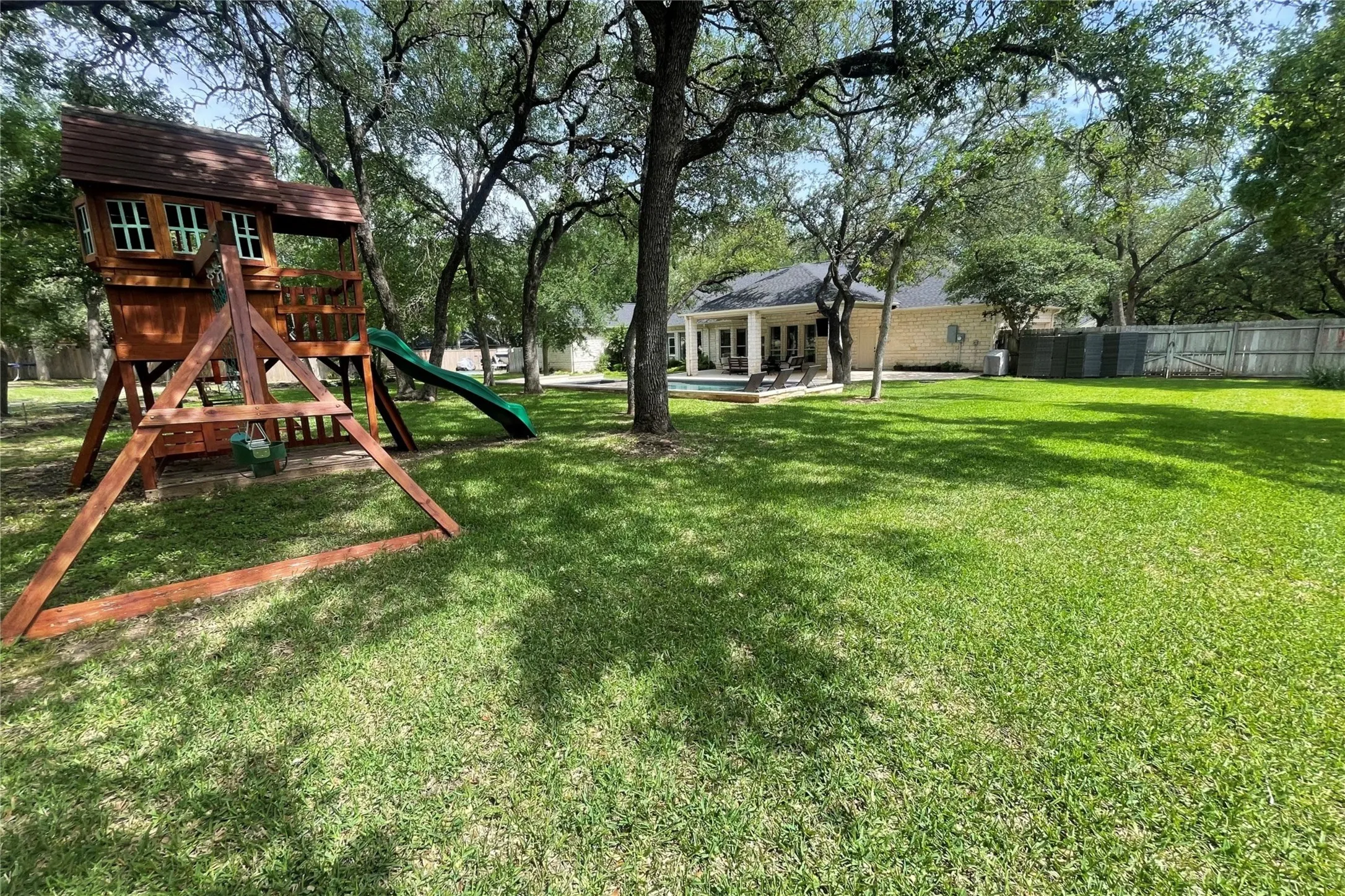 Expansive backyard featuring a lush lawn, mature trees, and a wooden play structure with a slide
