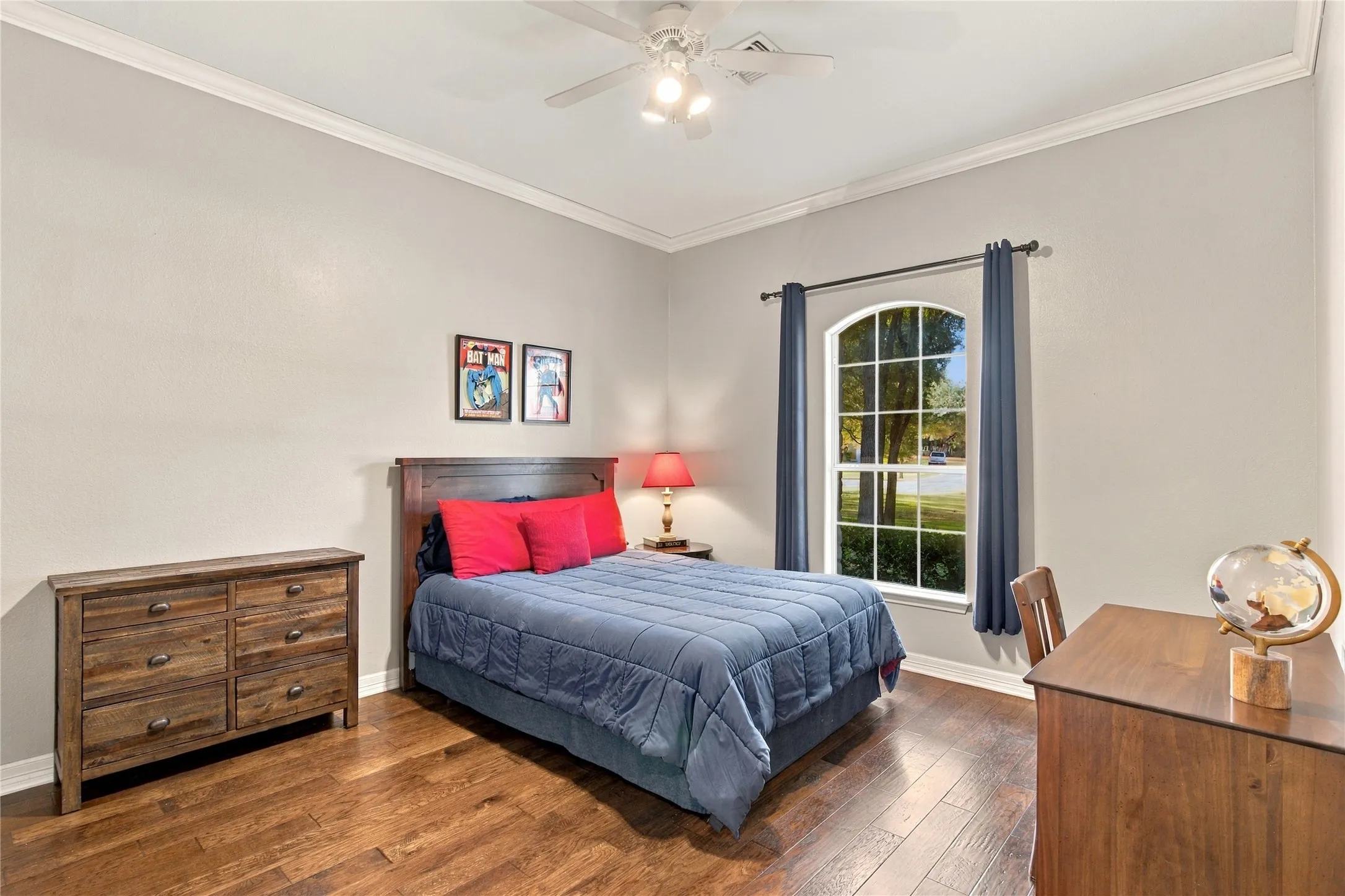 Arch-top window with grid pattern, wood-finish flooring, ceiling fan with integrated lighting, crown molding, and a solid wood headboard
