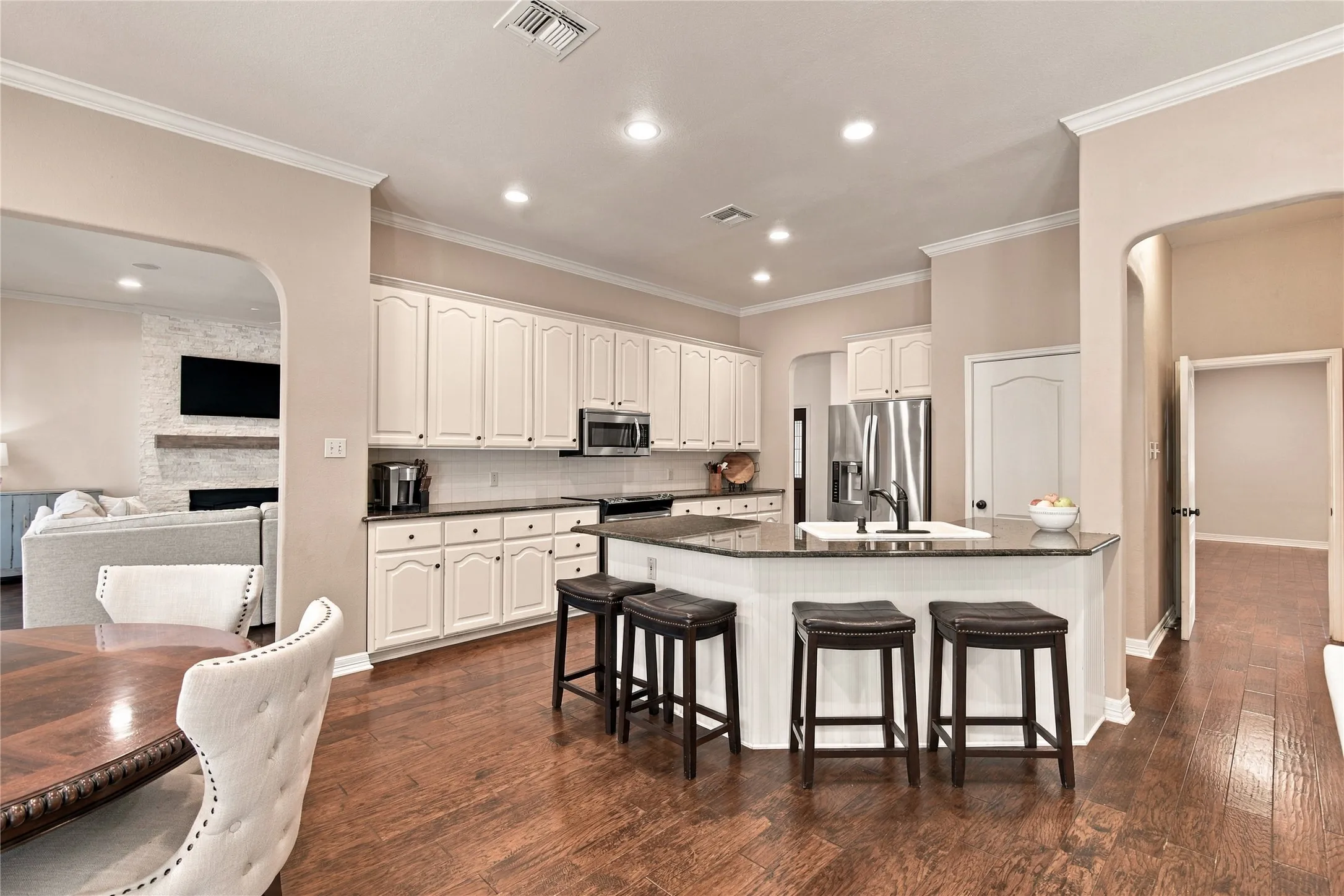 Kitchen featuring a central island with a built-in sink, white cabinetry, dark countertops, recessed lighting, and wood-finish flooring