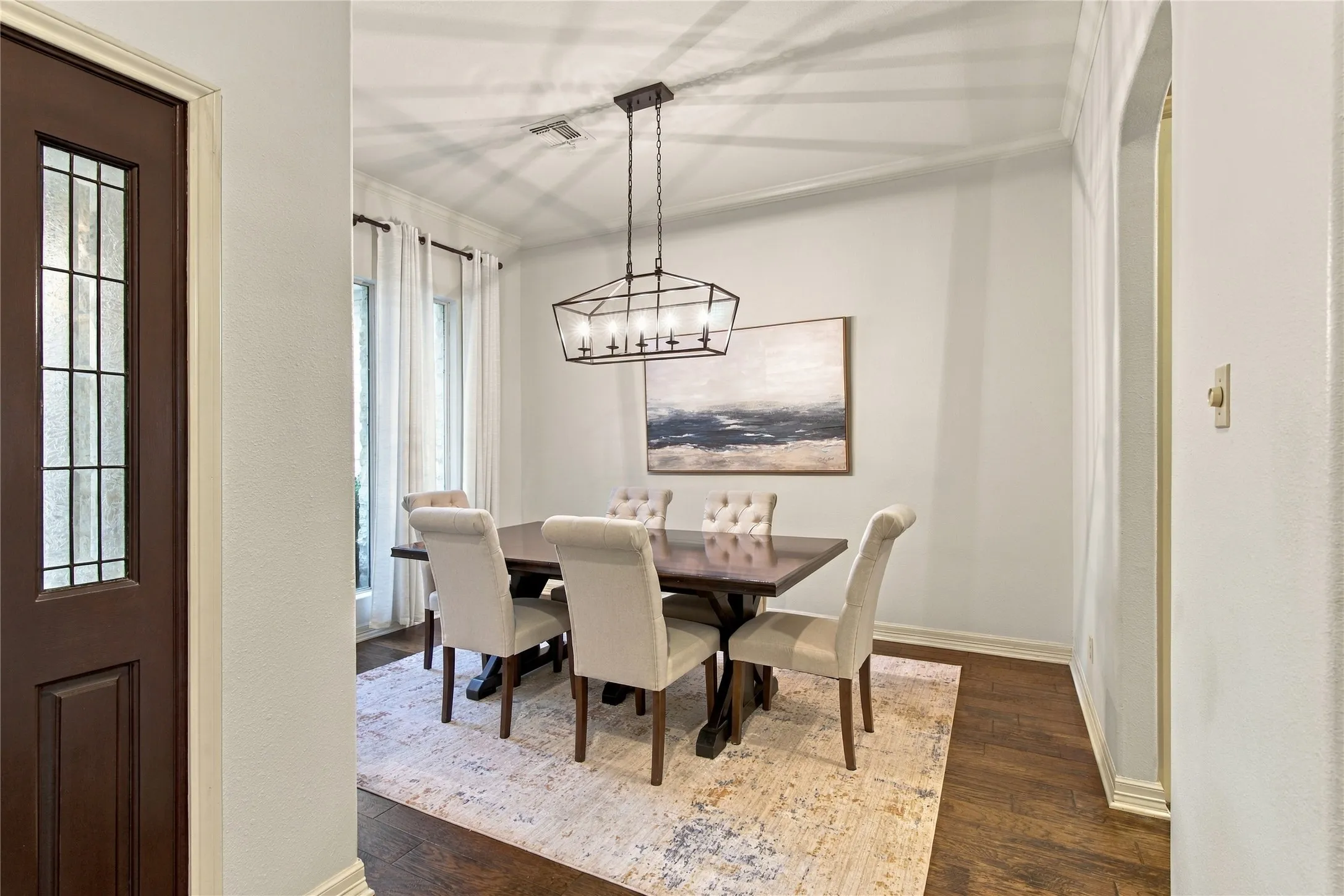 Formal dining area featuring rich wood-finish flooring, a contemporary linear chandelier, and expansive windows