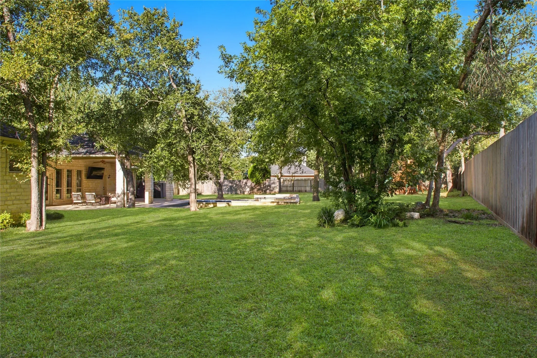 Expansive backyard featuring a manicured lawn, mature trees, and a privacy fence