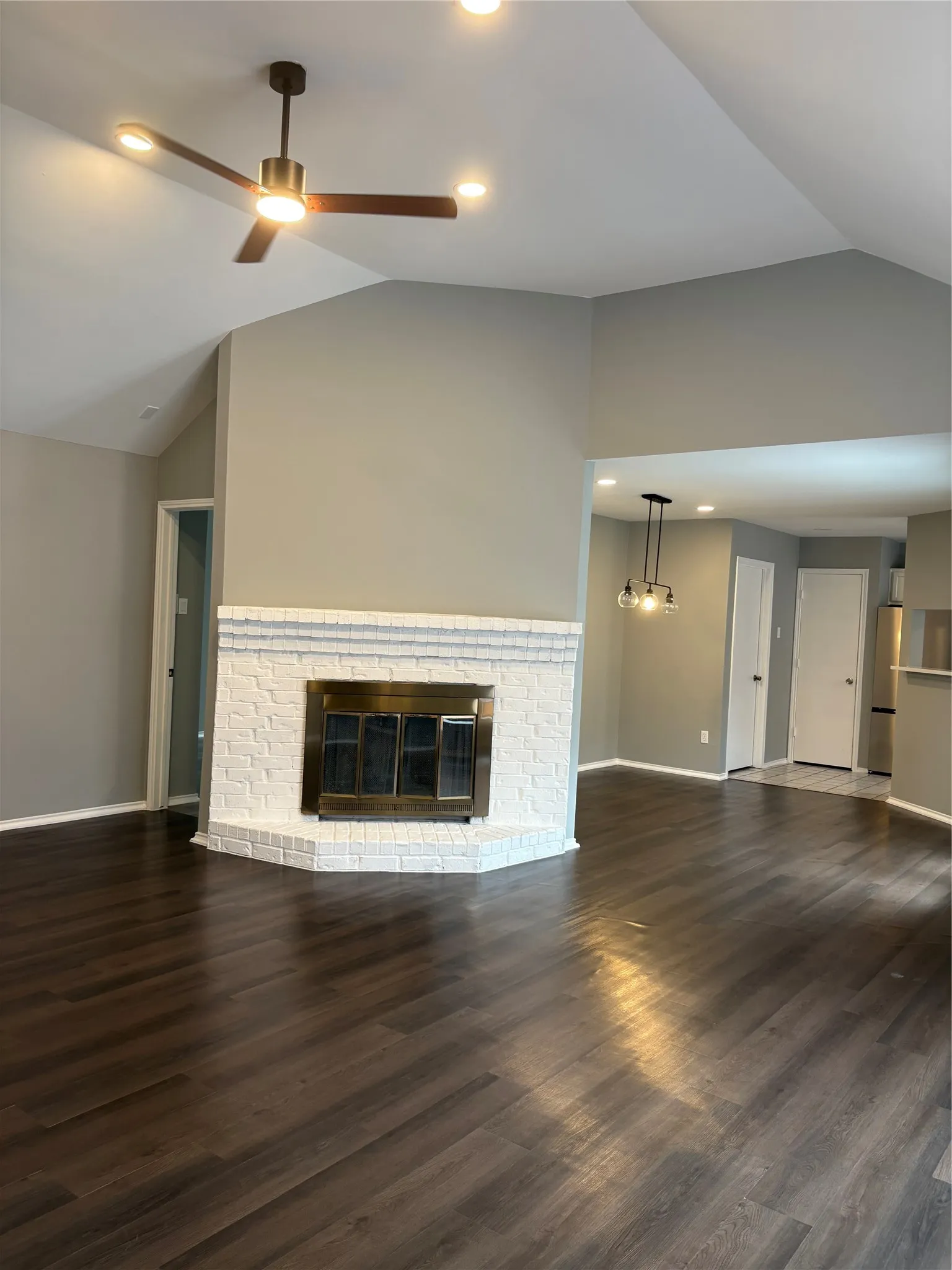 Vaulted ceiling with a ceiling fan, fireplace with a white brick surround, wood-finish flooring, and recessed lighting