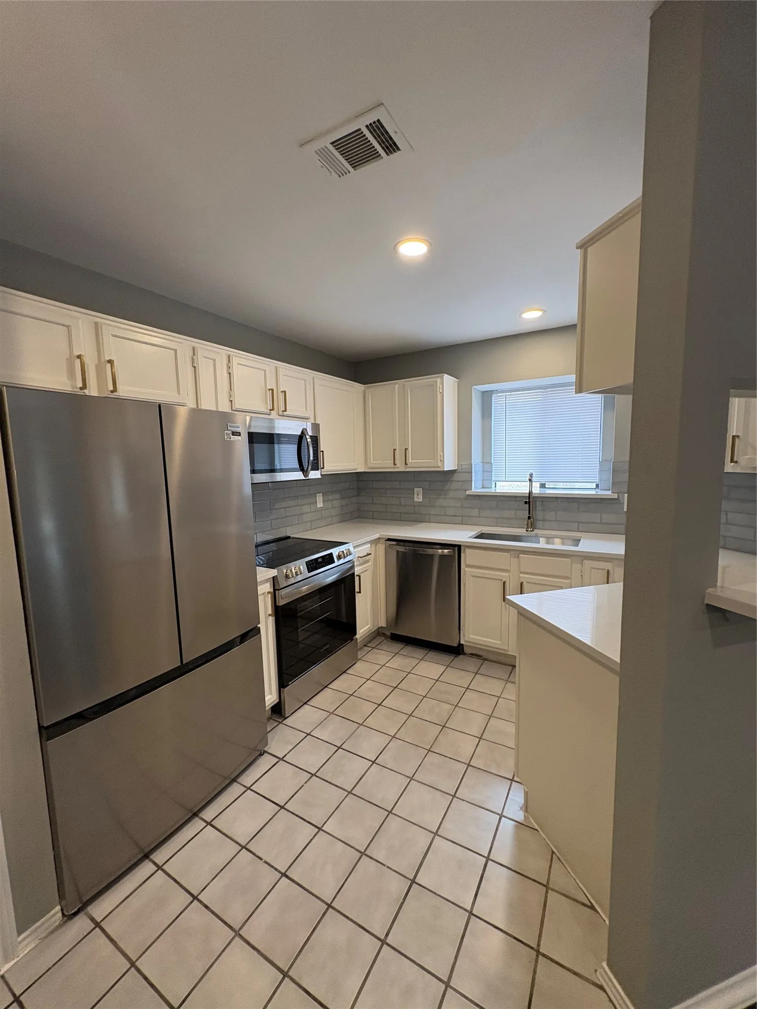 Stainless steel appliances, white cabinetry, tile flooring, light-toned countertops, and a subway tile backsplash