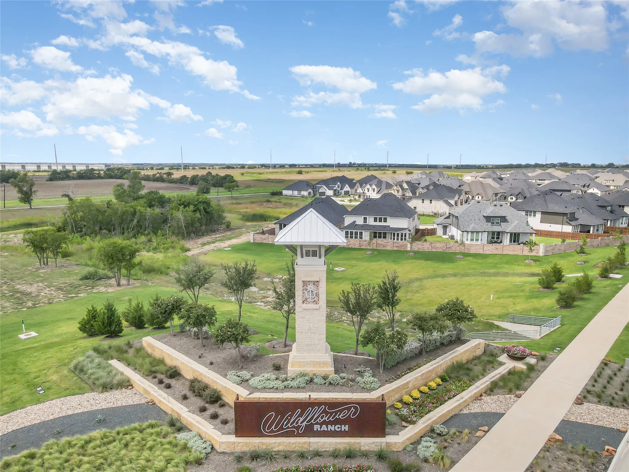 Community entrance featuring a stone monument with a pitched roof, landscaped beds, and a paved pathway