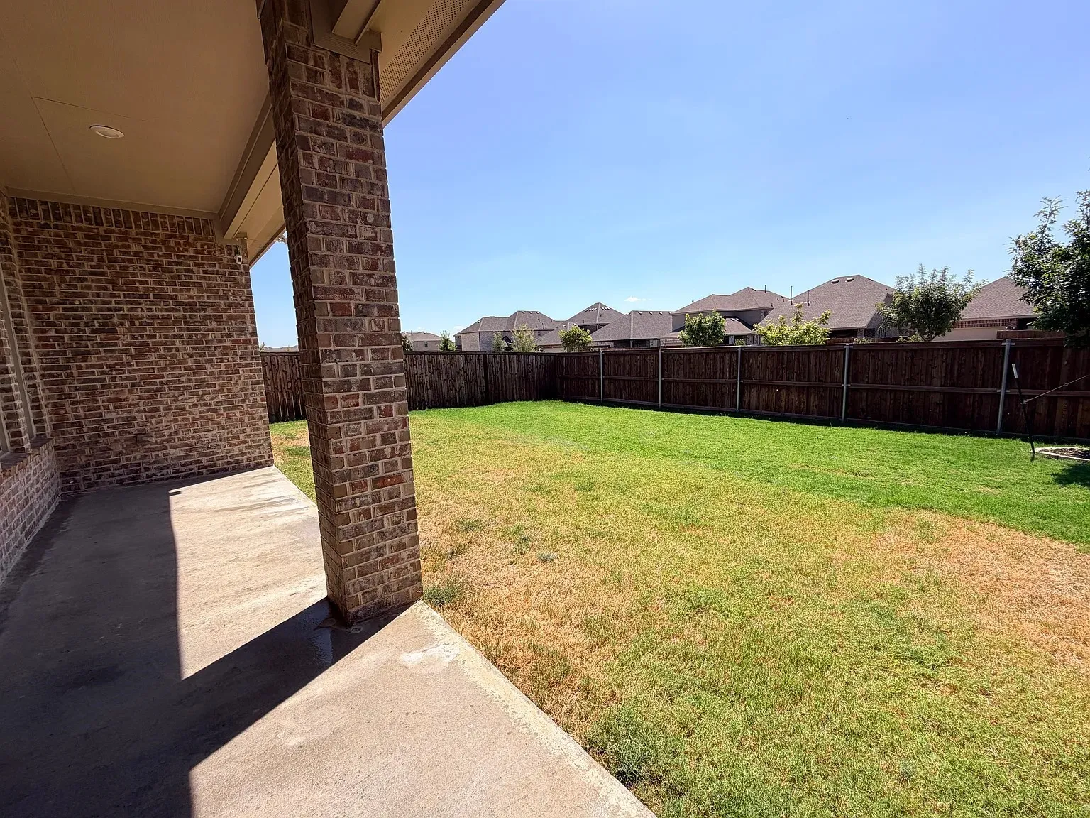 Expansive backyard featuring a privacy fence and a concrete patio with brick columns