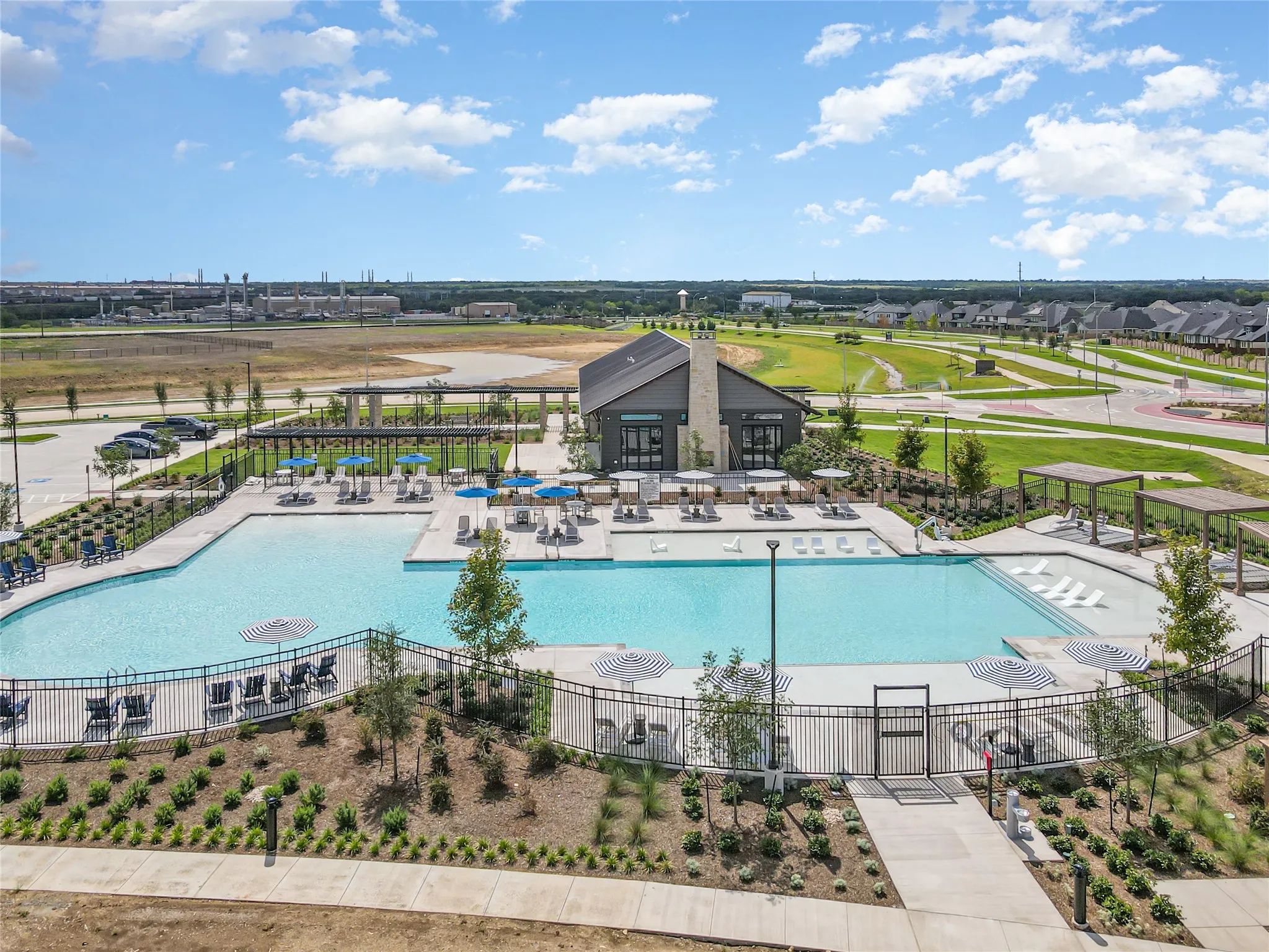 Expansive swimming pool with integrated tanning ledges, surrounded by a concrete deck and a black metal fence