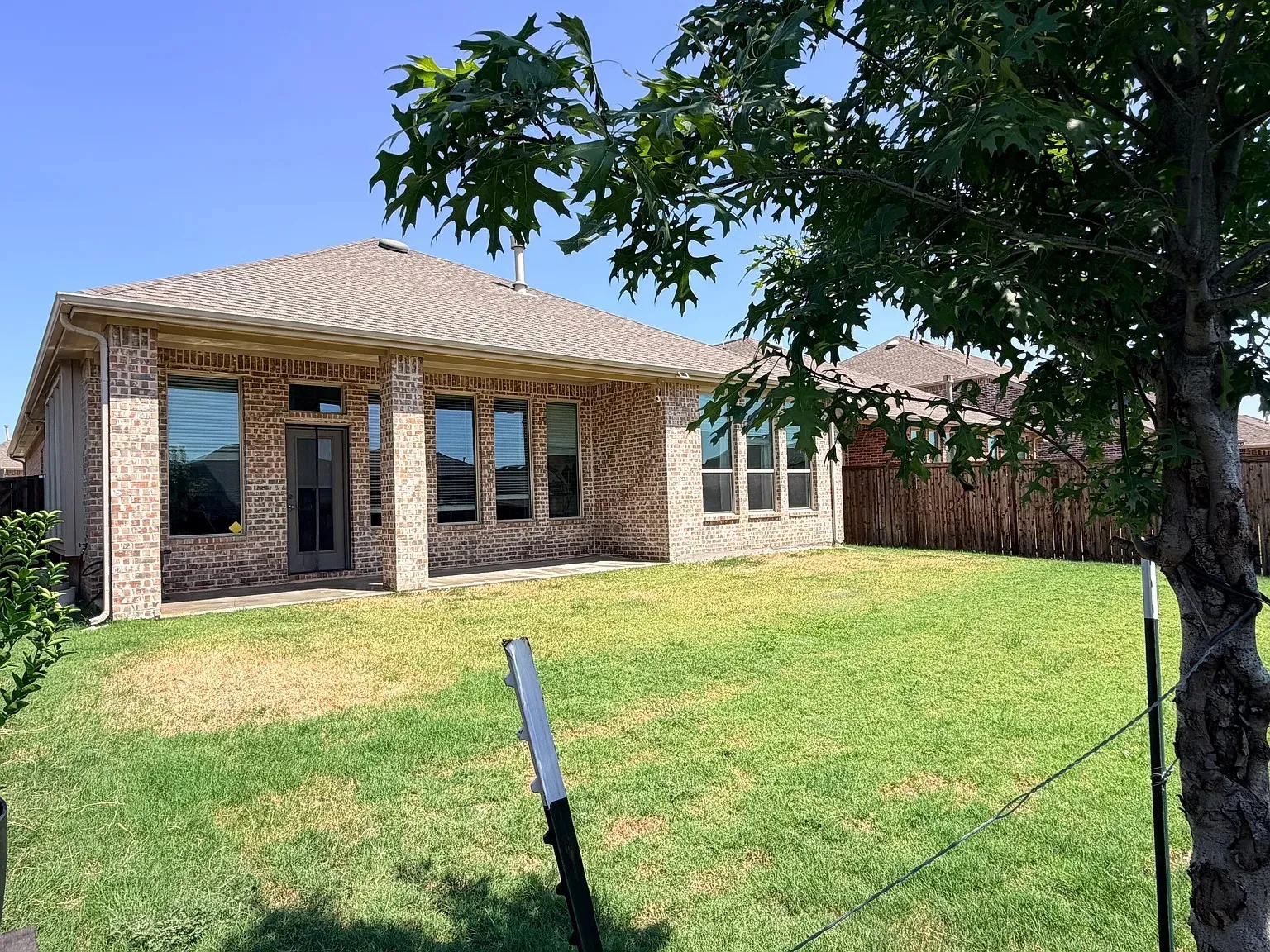 Brick exterior with multiple windows, covered patio, and a fenced backyard