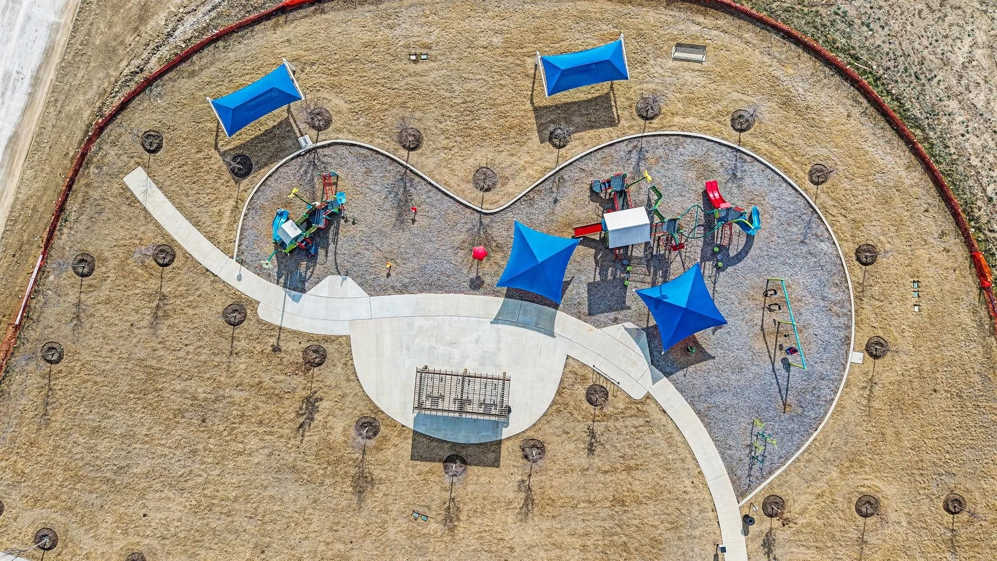 Community playground featuring multiple play structures, integrated shade canopies, paved pathways, and surrounding landscape planting