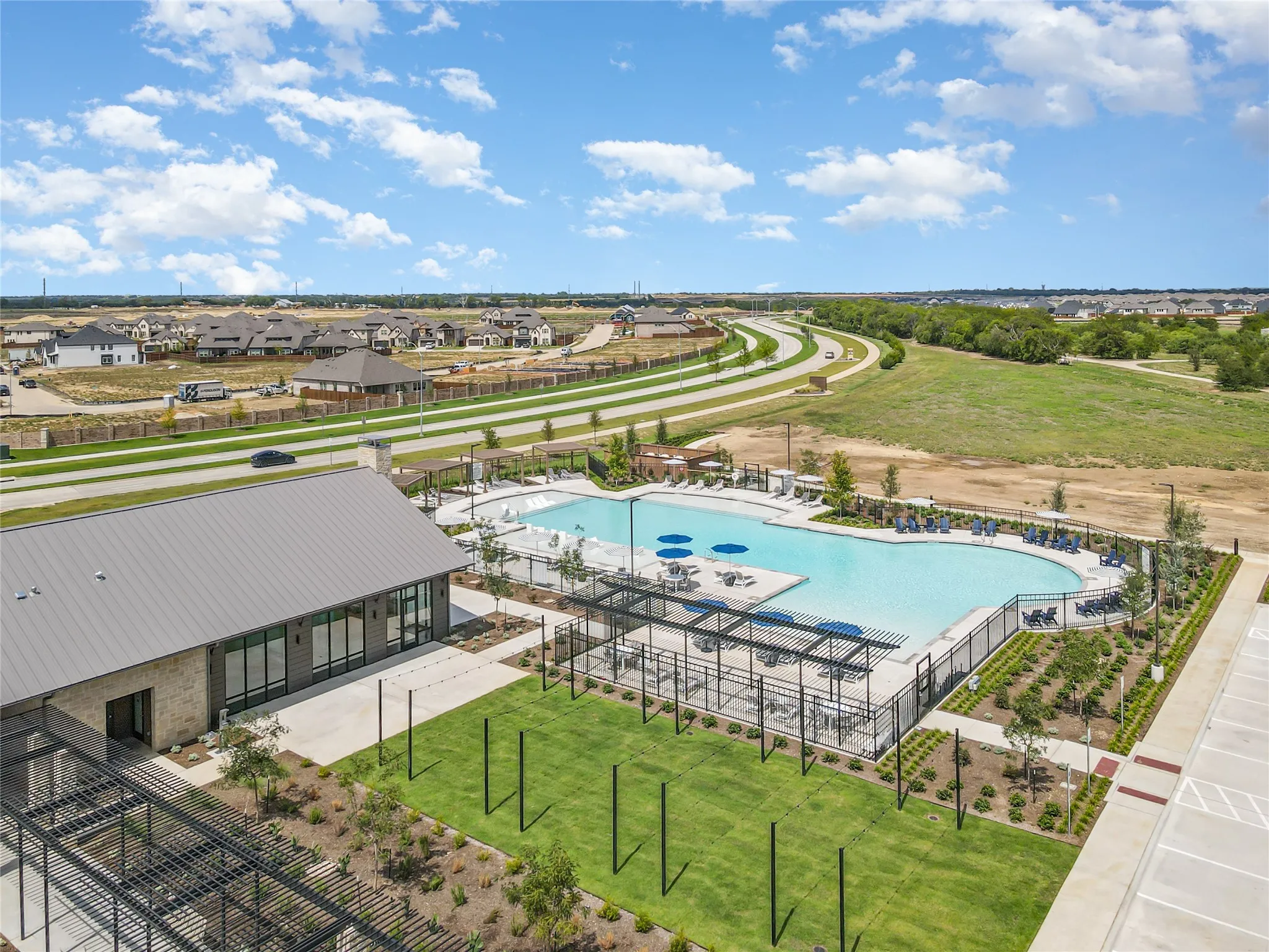 Resort-style pool with integrated lounging areas, extensive paved deck, and adjacent clubhouse building with a metal roof