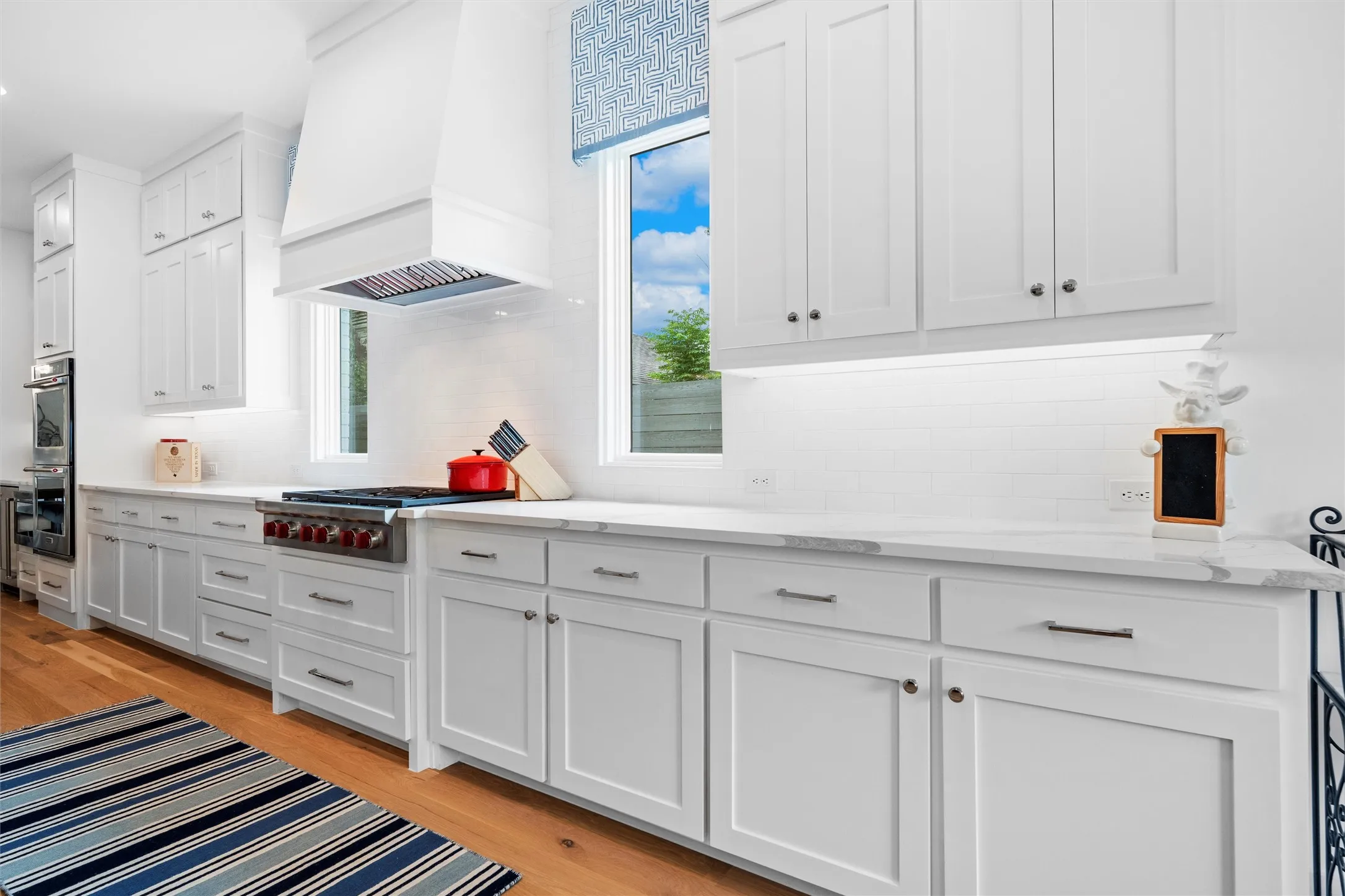 Kitchen with backsplash, light hardwood / wood-style flooring, premium range hood, and white cabinetry