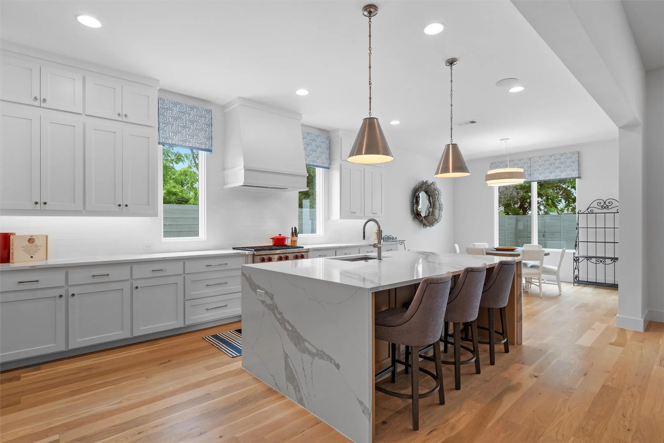 Kitchen featuring light hardwood / wood-style floors, plenty of natural light, hanging light fixtures, and custom range hood.  Notice the extensive use of quartz, especially the waterfall feature on the island.