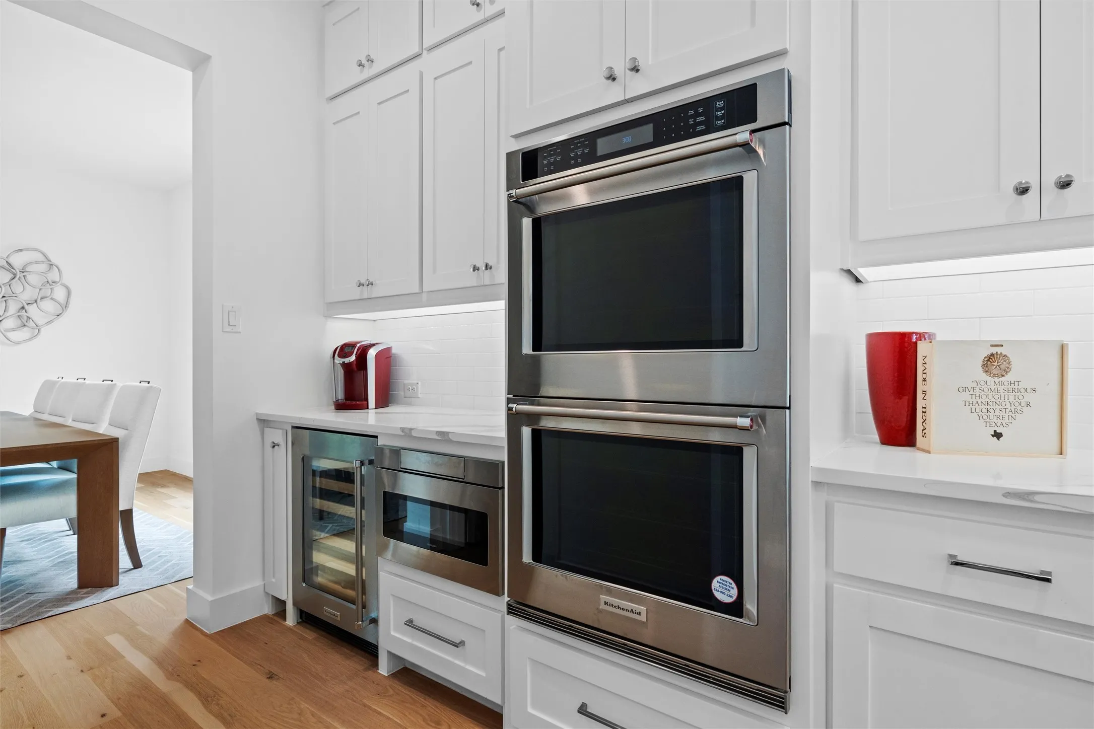 Kitchen featuring double ovens, tasteful backsplash, wine cooler, white cabinetry, and light wood-type flooring
