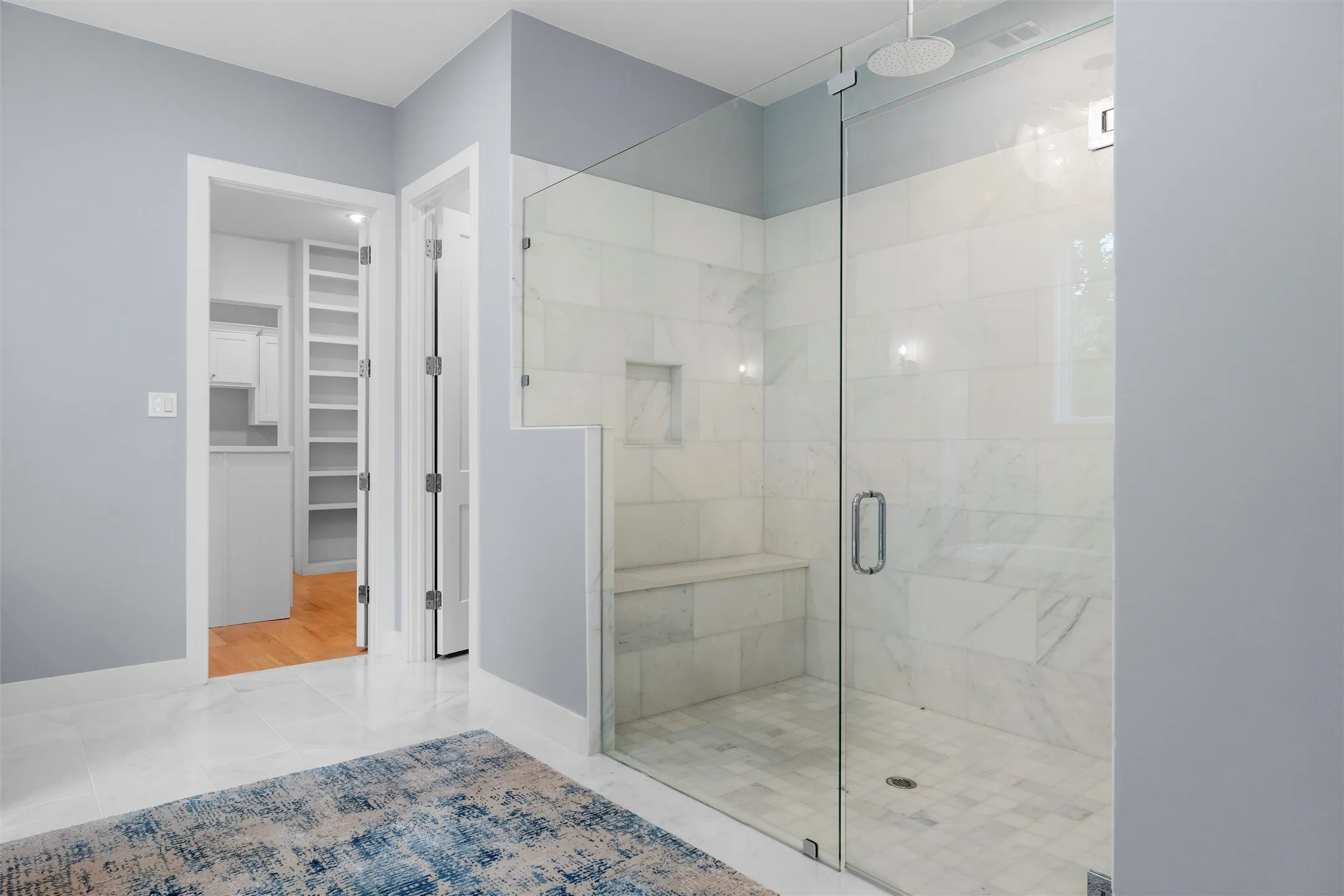 Master bathroom, extra large shower with marble walls, seat, and rain shower head.