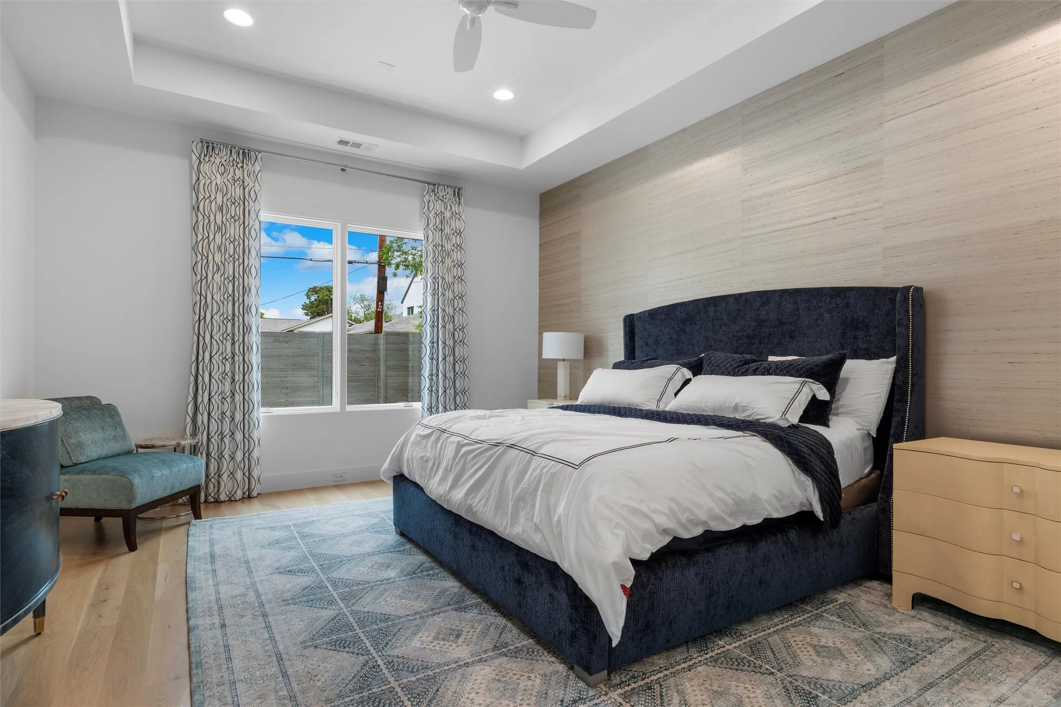 Master bedroom featuring wood-type flooring, ceiling fan, and a tray ceiling with large windows overlooking the beautiful pool.