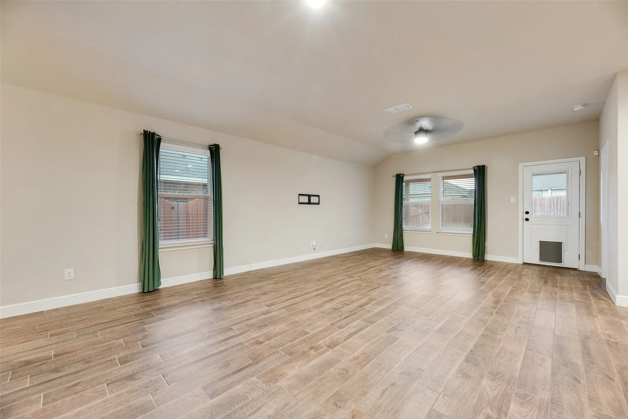 Spacious room featuring wood-finish flooring, two windows with blinds, a ceiling fan, and a rear exterior door