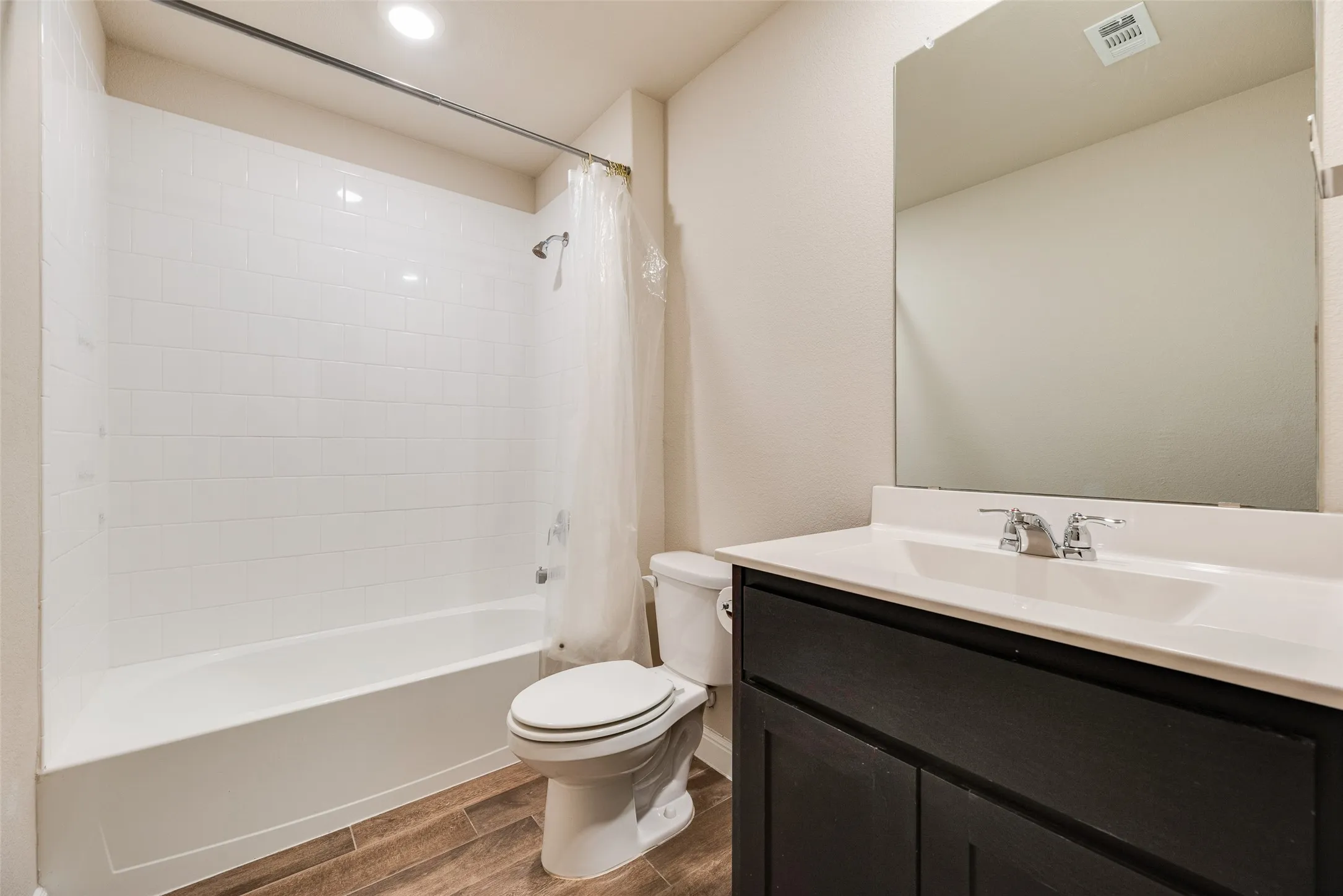 White subway tile shower surround, integrated tub, wood-finish flooring, dark wood-finish vanity with white sink, and chrome fixtures