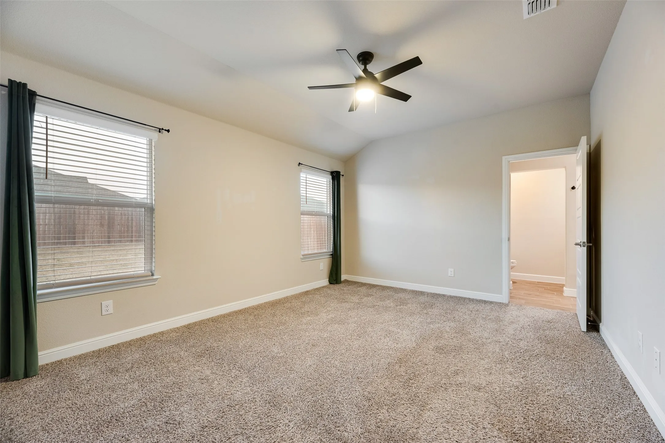 Vaulted ceiling with a ceiling fan, plush carpet flooring, and multiple windows