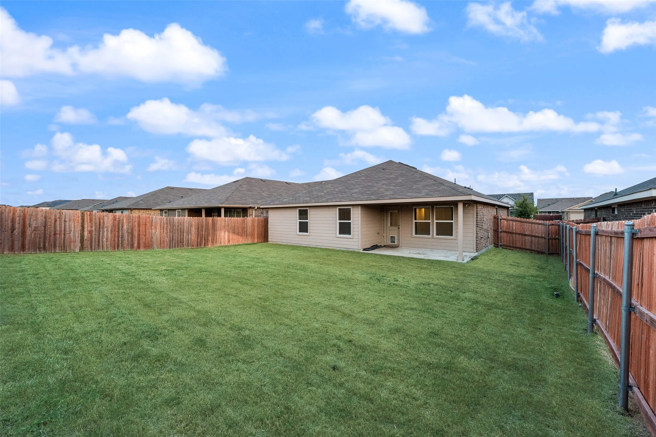 Spacious backyard featuring a manicured lawn, wood fencing, and a covered concrete patio