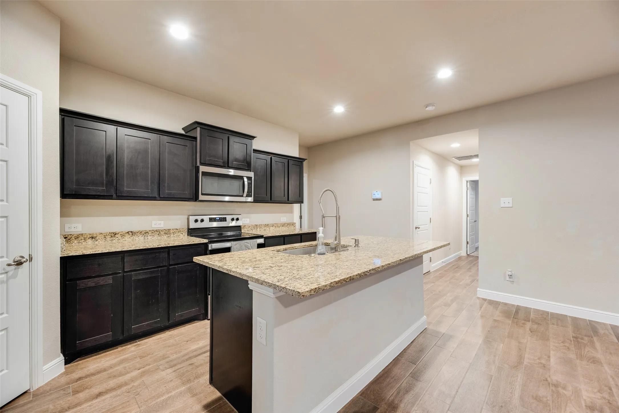 Kitchen featuring dark wood cabinetry, light-toned countertops, stainless steel appliances, and wood-finish flooring