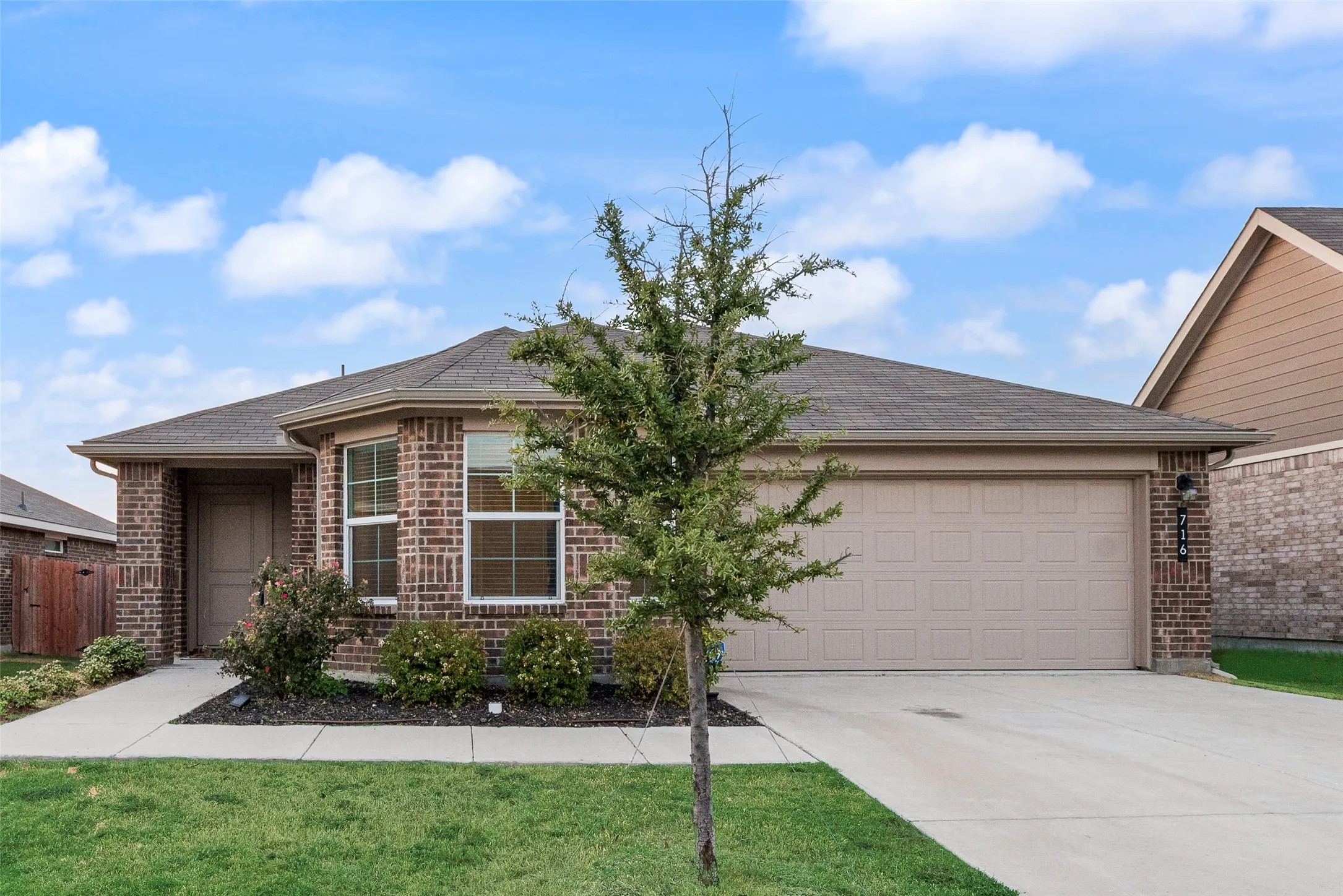 Brick exterior with a peaked roofline, an attached garage with a panel door, a concrete driveway, and established front landscaping