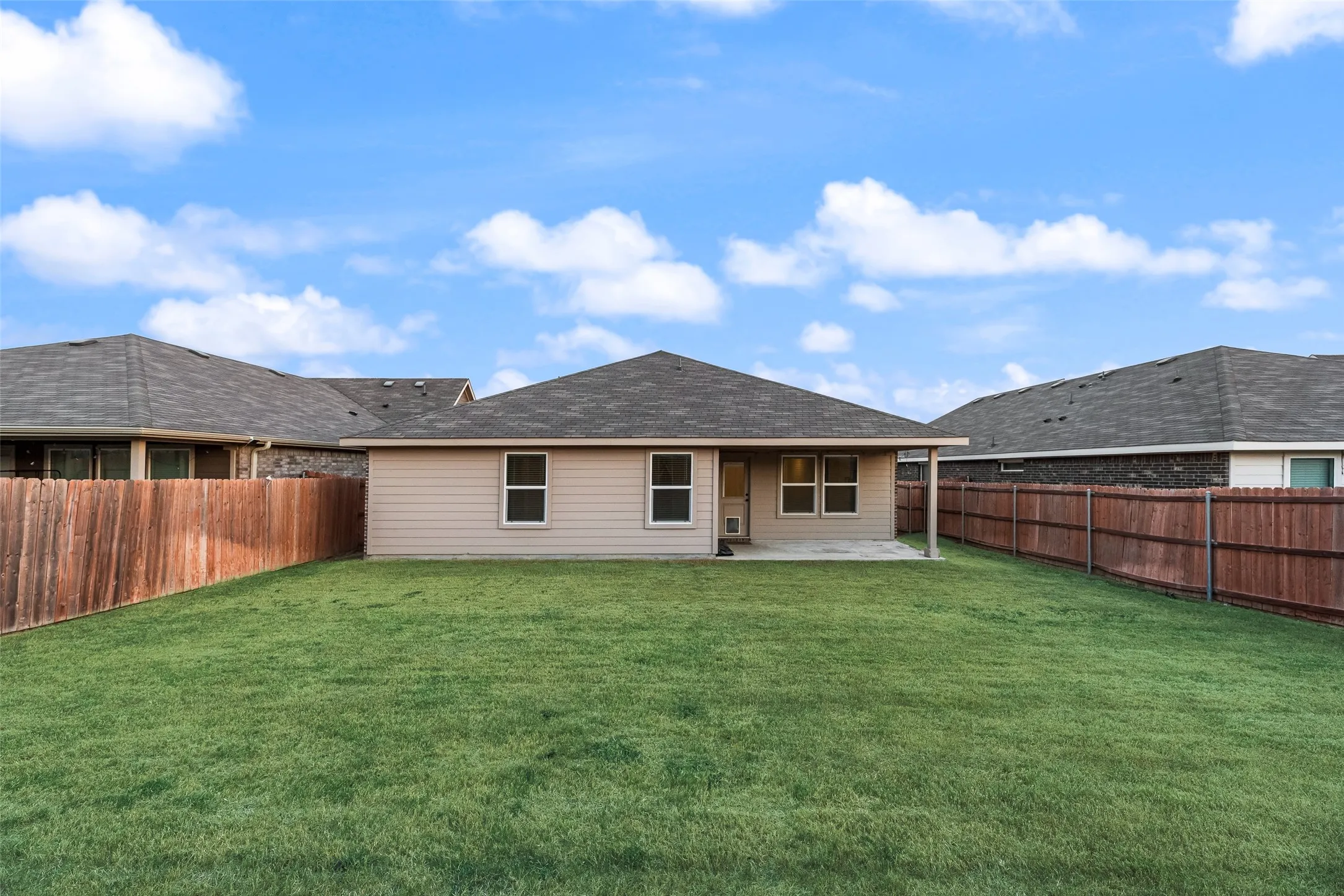 Expansive backyard with a flat lawn, privacy fencing, and a covered patio area