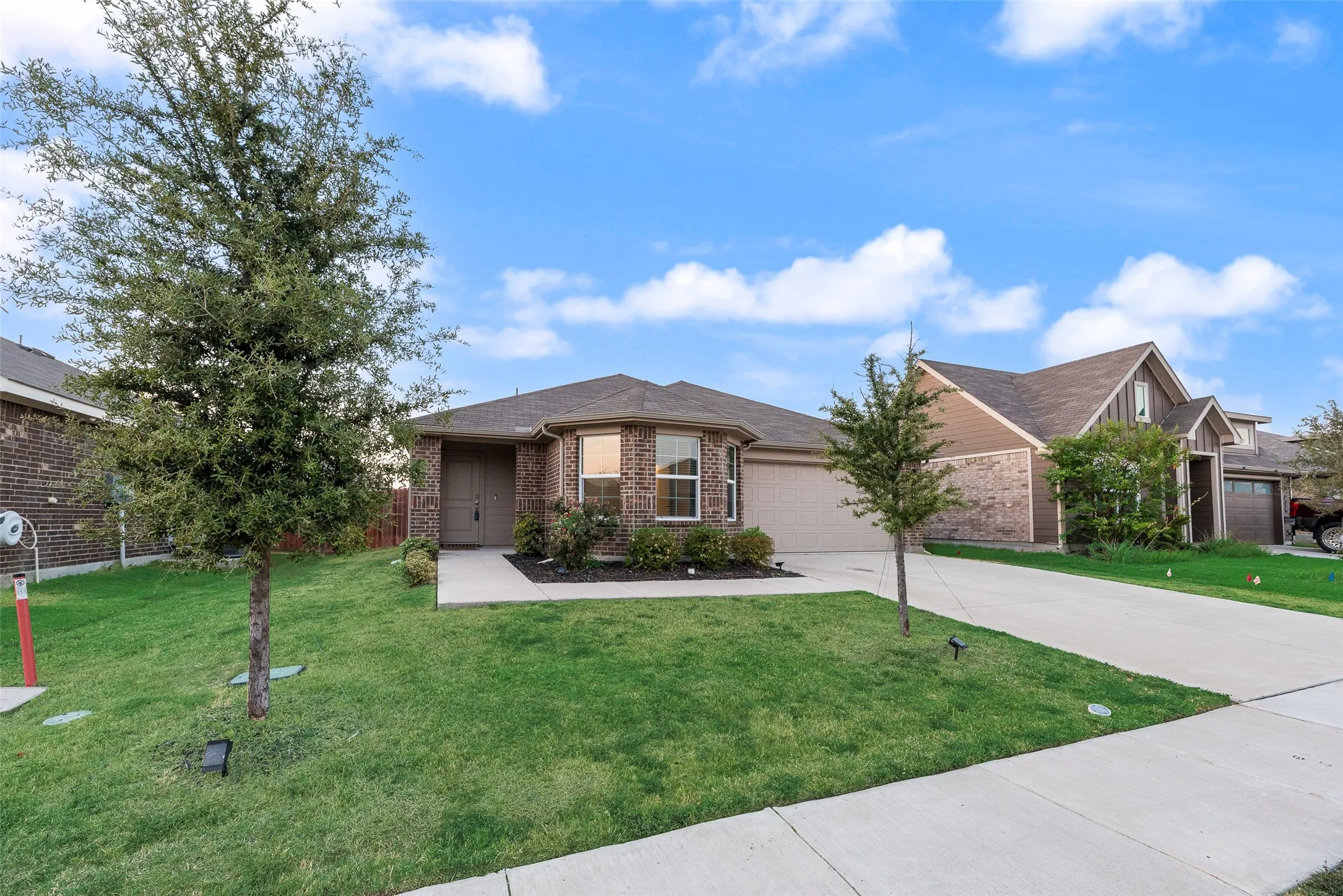 Brick exterior with an attached garage, concrete driveway, and front yard landscaping