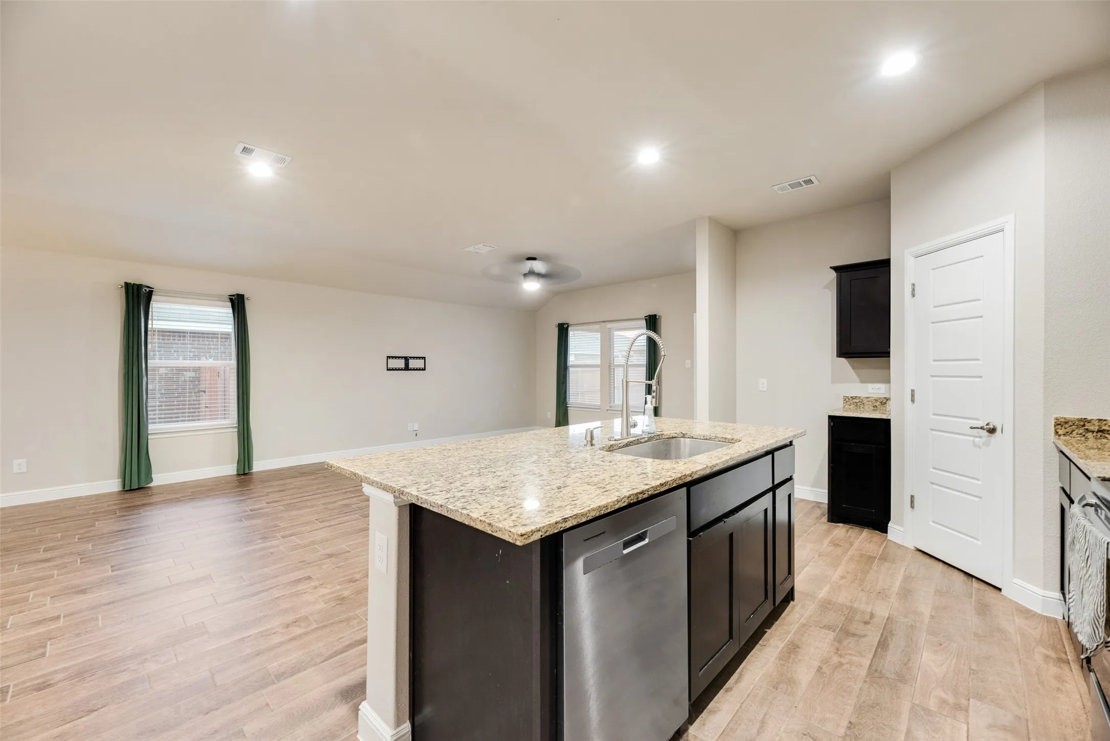 Open-concept living space featuring wood-finish flooring, recessed lighting, and a kitchen island with stone countertops and an integrated sink