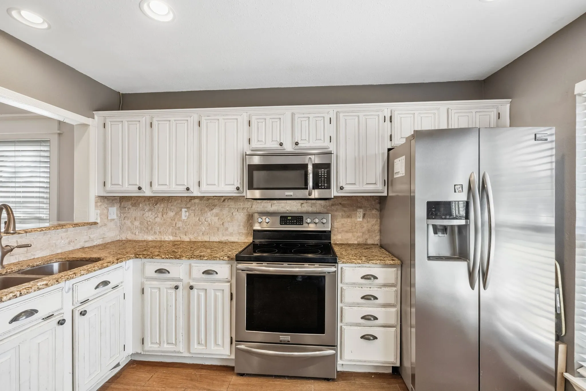 White cabinetry, stainless steel appliances, speckled countertops, and a tile backsplash