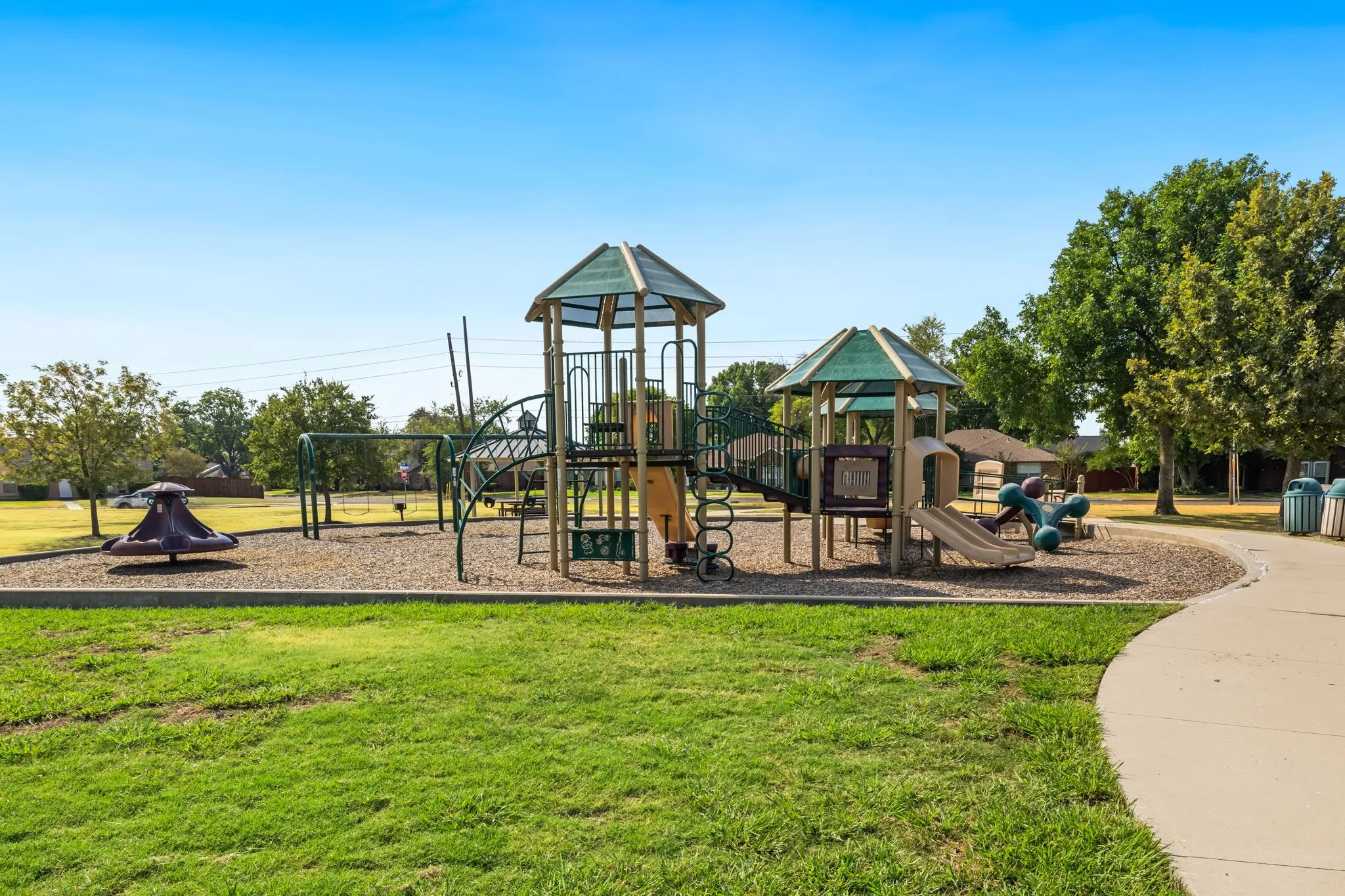 Friendship Park is just a short walk down the street. Paved walkway leading to a playground area with a covered gazebo, picnic tables, and a basketball court.