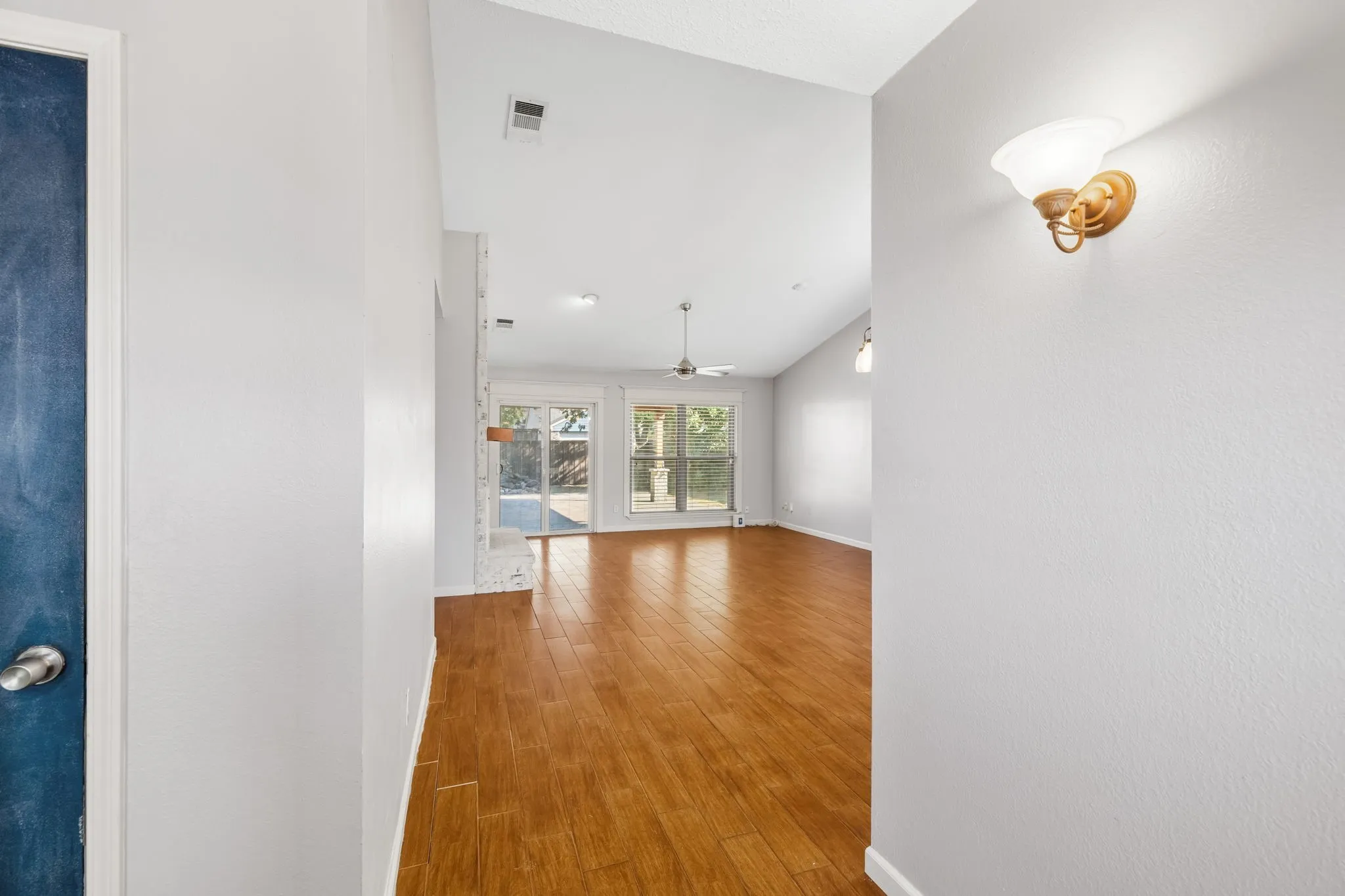 View from front door looking across open floor plan of dining-living room combo, and toward the back yard. Vaulted ceilings, LVP wood-finish flooring, and a ceiling fan