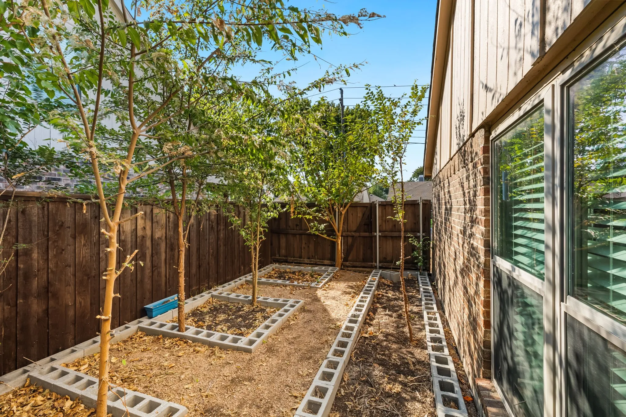 Fenced yard featuring mature trees, wood privacy fence, and concrete block garden beds. Bring your gardening ideas!
