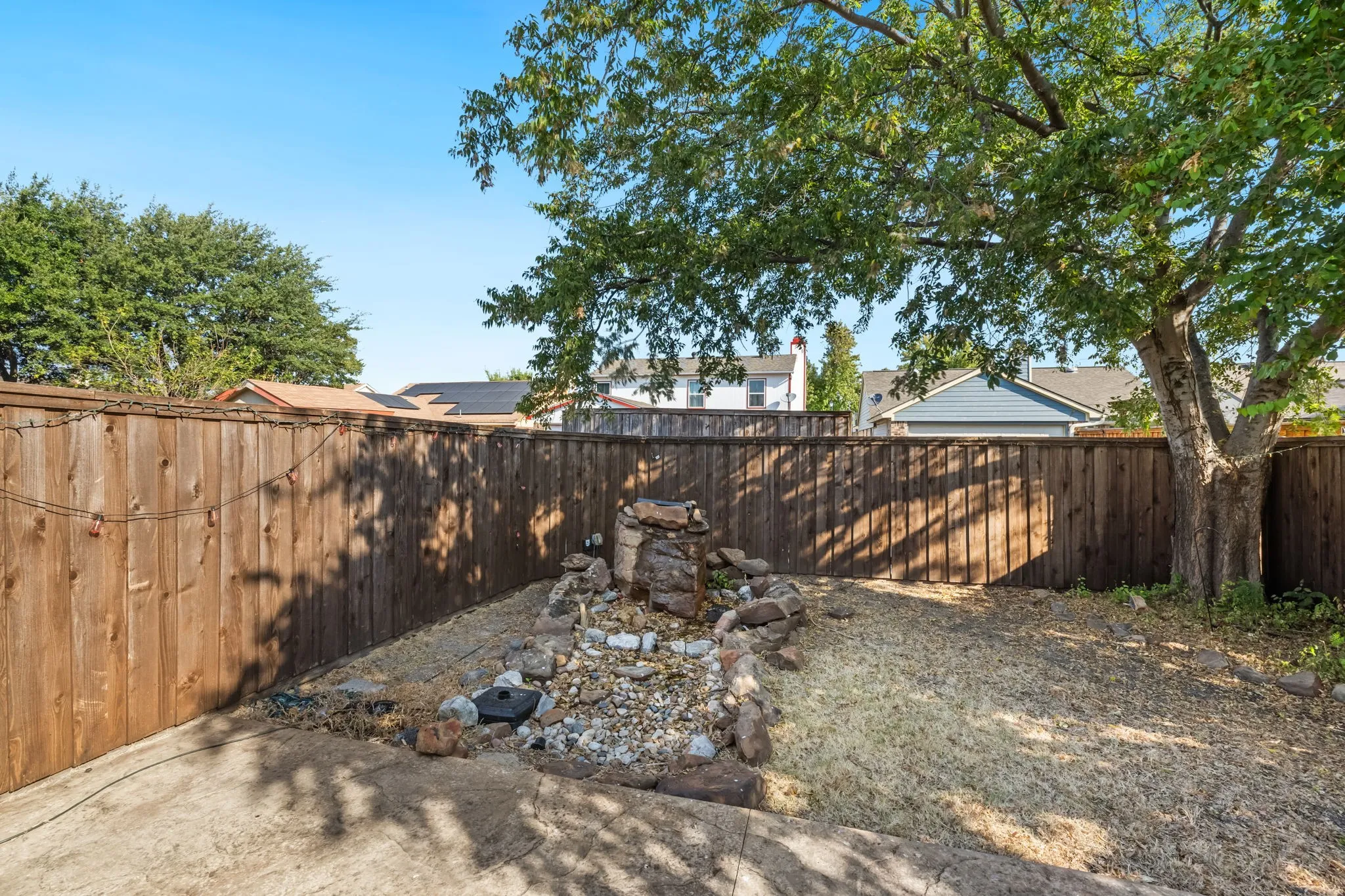 Private backyard space featuring a wood fence, mature tree, and a rock water feature