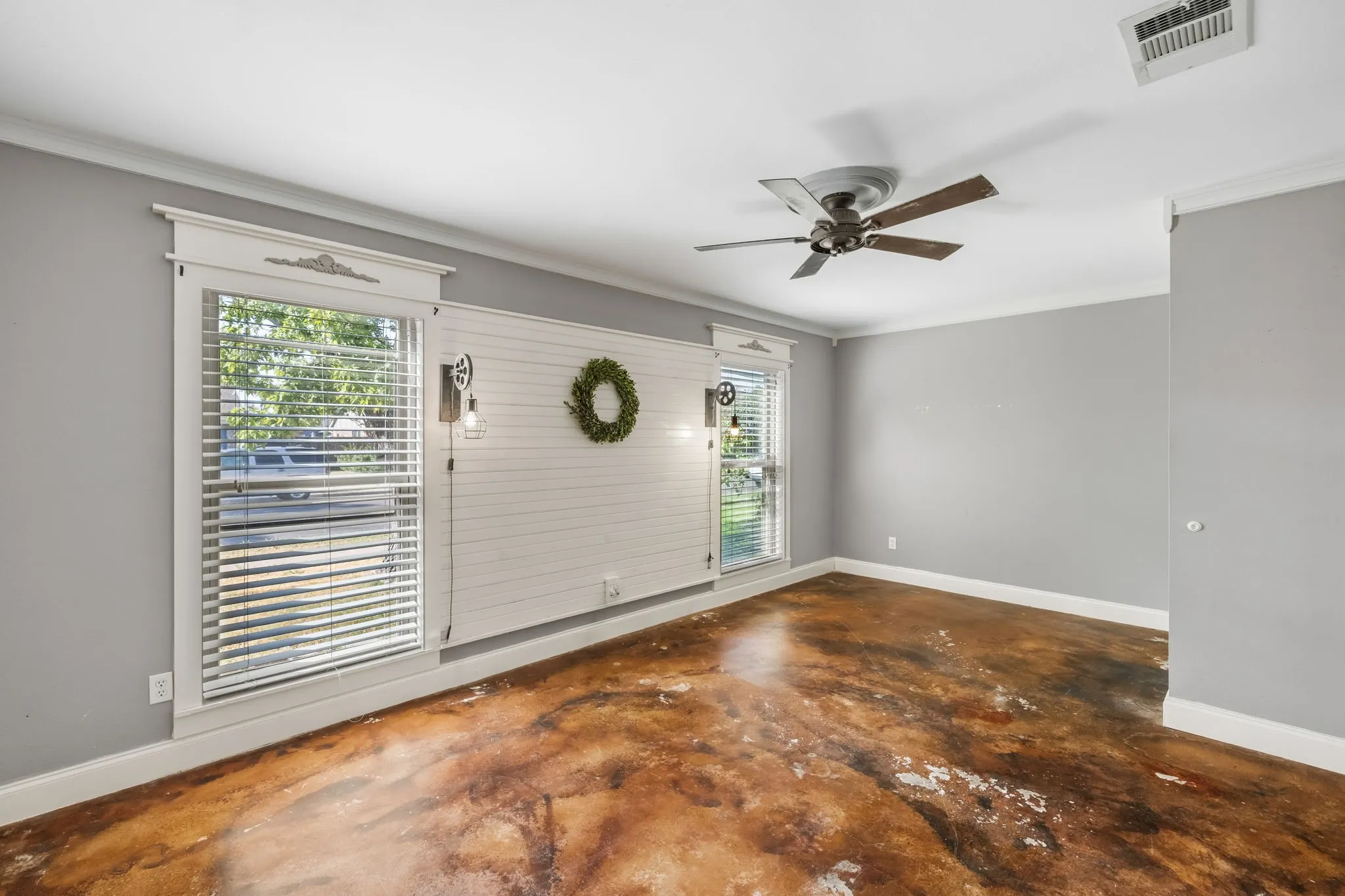 Primary bedroom with stained concrete flooring, dual windows, and shiplap accent wall.