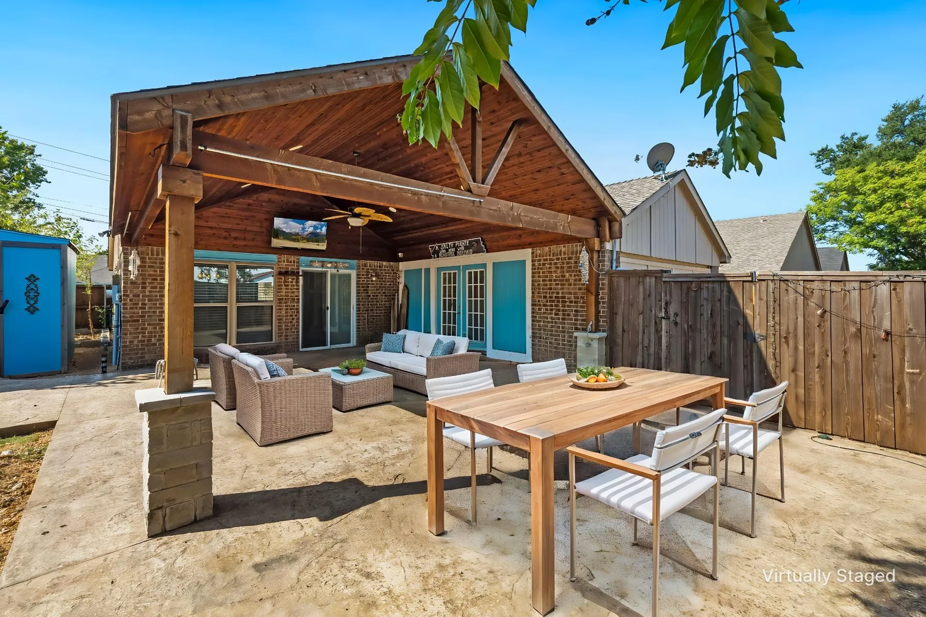 Virtually staged photo - showcasing what your outdoor entertainment space could look like. Expansive concrete patio featuring a wood-covered outdoor living area, wood beam supports, a brick exterior, and a wood privacy fence