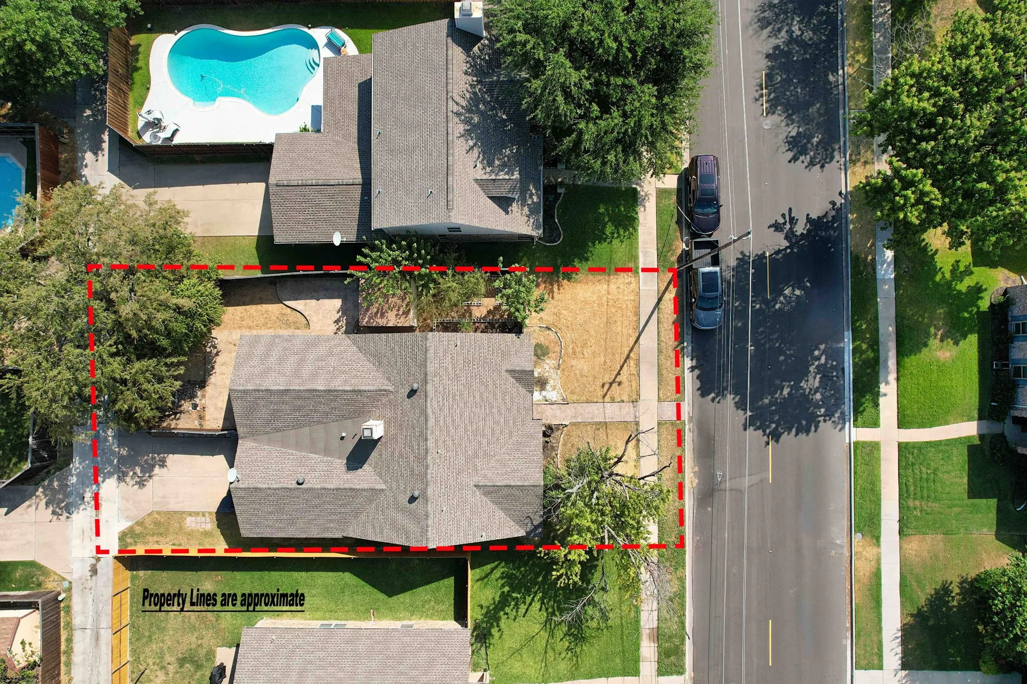 Aerial perspective showcasing a residential property with a shingle roof and mature trees, featuring a concrete driveway and sidewalk access. Property boundary is approximate.