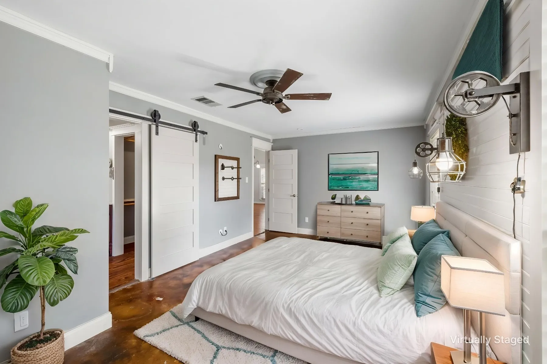 Virtually staged photo - Primary bedroom. Smooth stained concrete flooring, barn door entry to en suite, ceiling fan with integrated lighting, shiplap accent wall, and wall-mounted industrial-style lighting