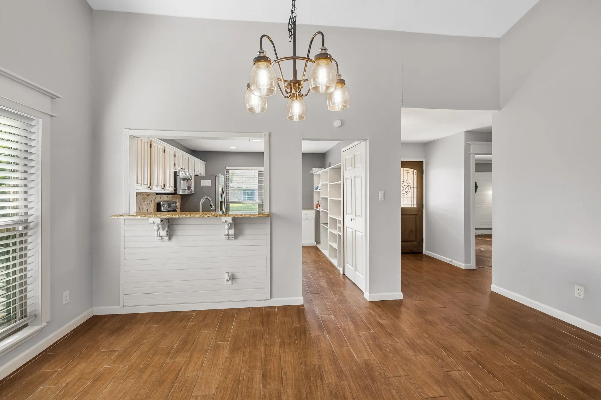 View from the living room area toward the dining room, kitchen with pass-through window, front entry, and primary bedroom.