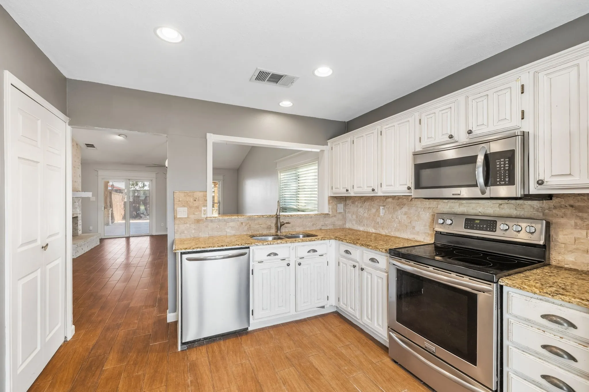 Kitchen featuring white cabinetry, granite countertops, stainless steel appliances, built-in microwave, pantry, and LVP flooring. Pass-through window provides convenience to the dining room.