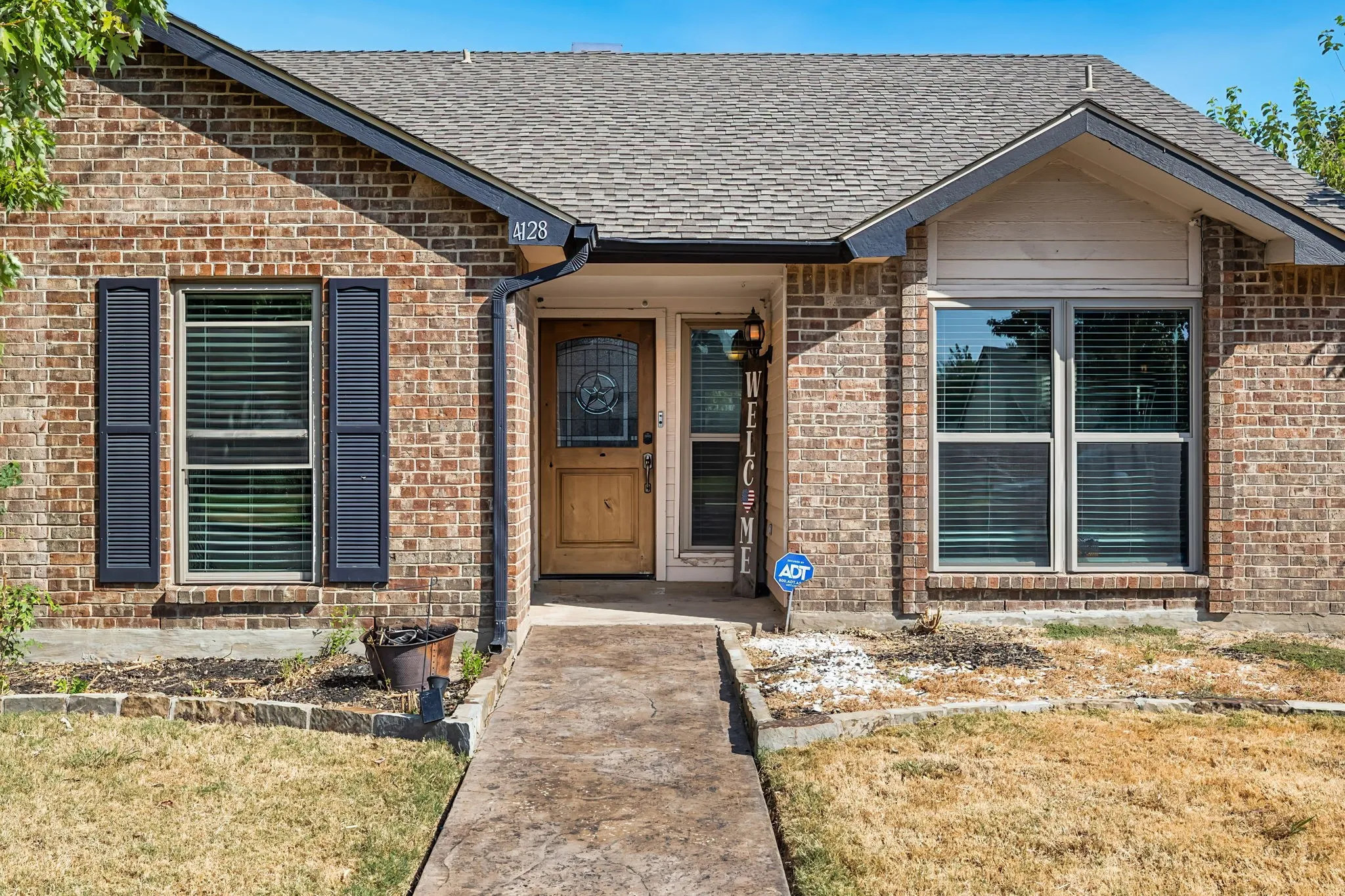 Brick exterior with a gabled roofline, featuring a natural wood front door with a decorative glass insert, and a concrete walkway