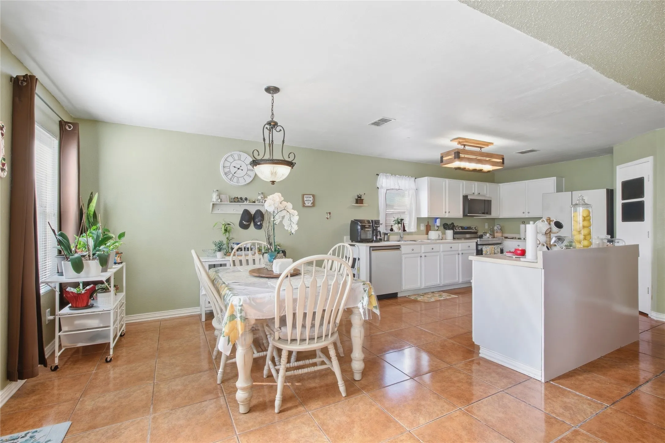 Tiled flooring throughout, an open-concept layout, white kitchen cabinetry, a built-in microwave, and a decorative pendant light fixture
